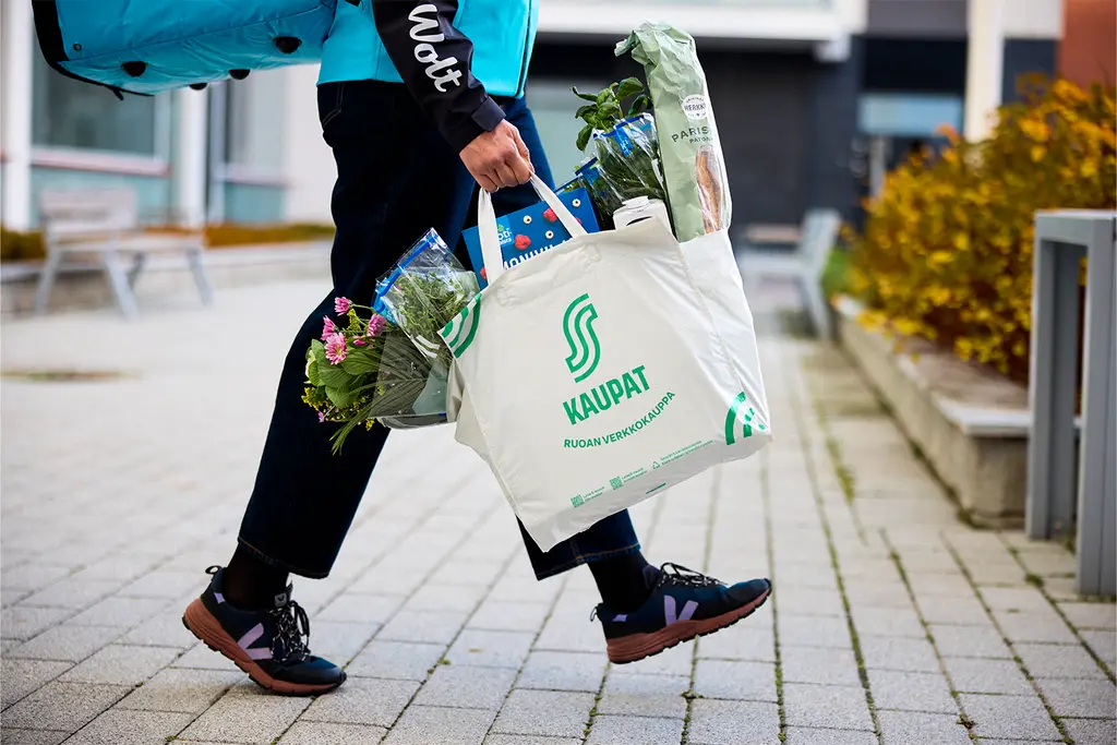 Wolt-kuriiri kantaa S-kaupat-kangaskassia, jossa on kukkia ja yrttejä.