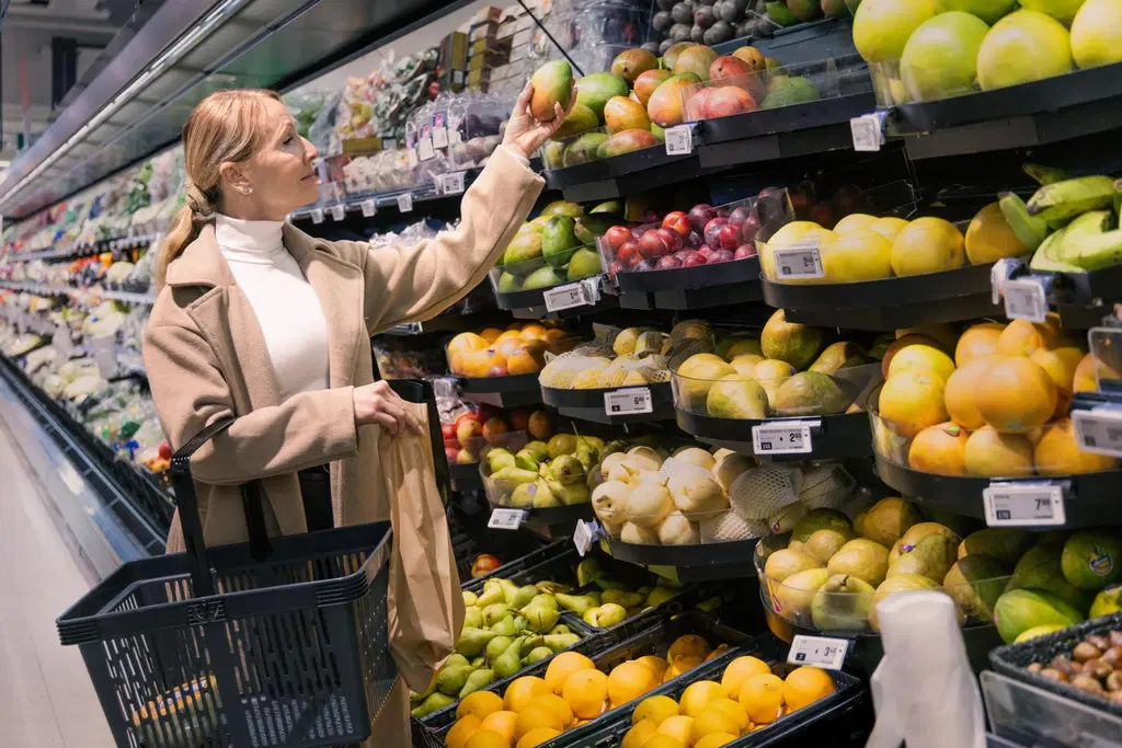 Asiakas kurottaa ottamaan mangon vihannes- ja hedelmäosaston hyllyltä. 