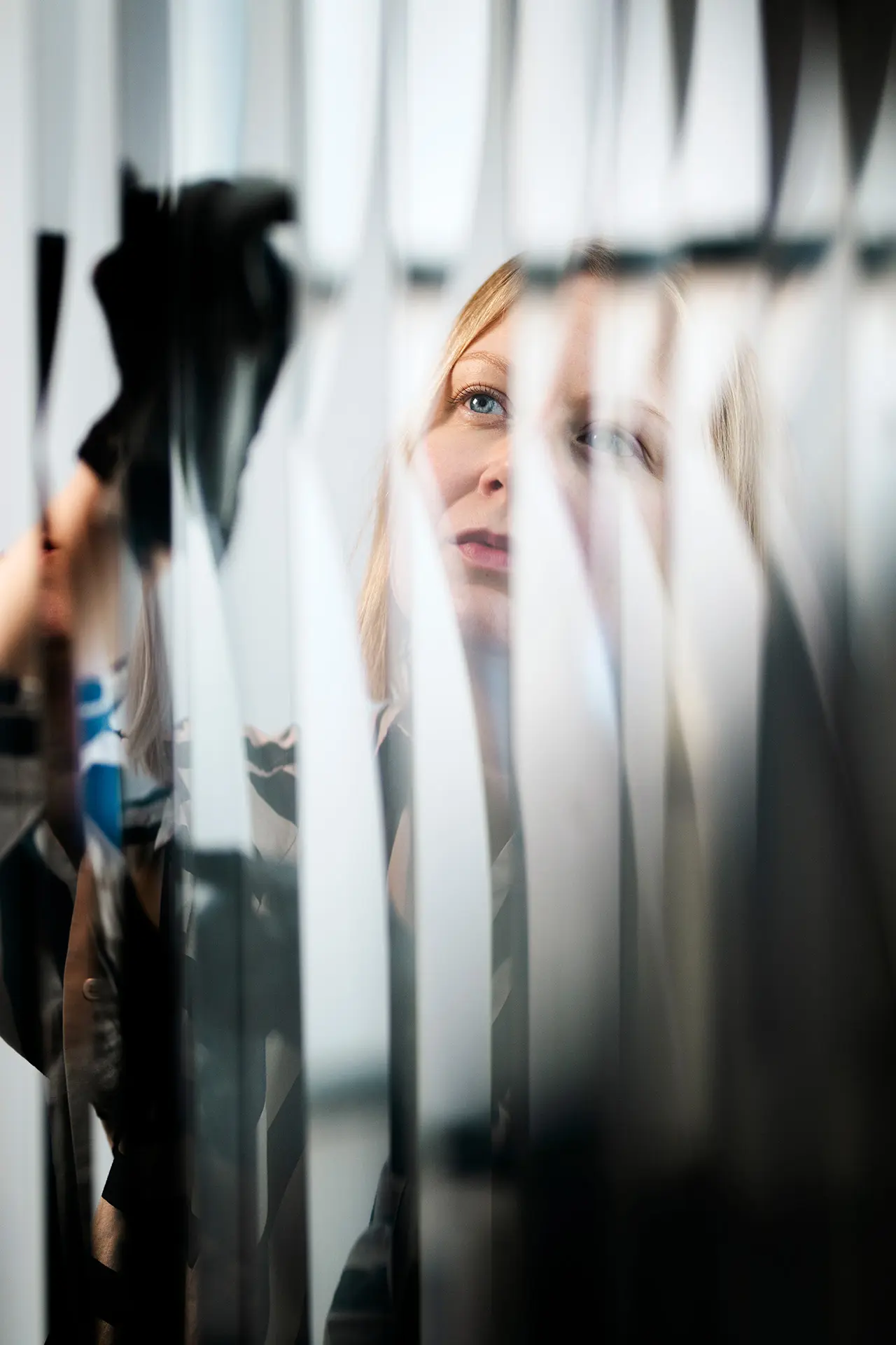 Konservaattori Liisa Vesa pyyhkii pölyjä taideteoksesta, jossa on pitkiä metallilevyjä.