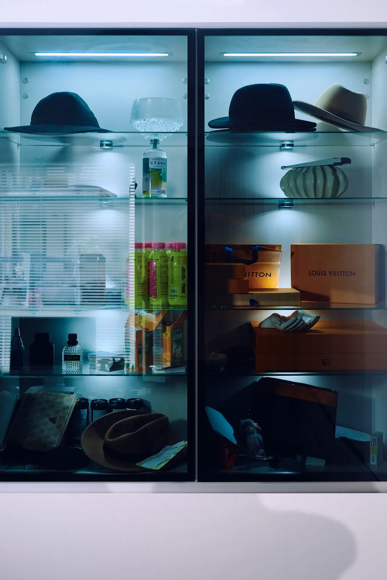 Vitriini, jossa on erilaisia hattuja ja asusteita, hajuvesipulloja, Louis Vuittonin oransseja tuotepakkauksia ja urheilujuomapulloja.