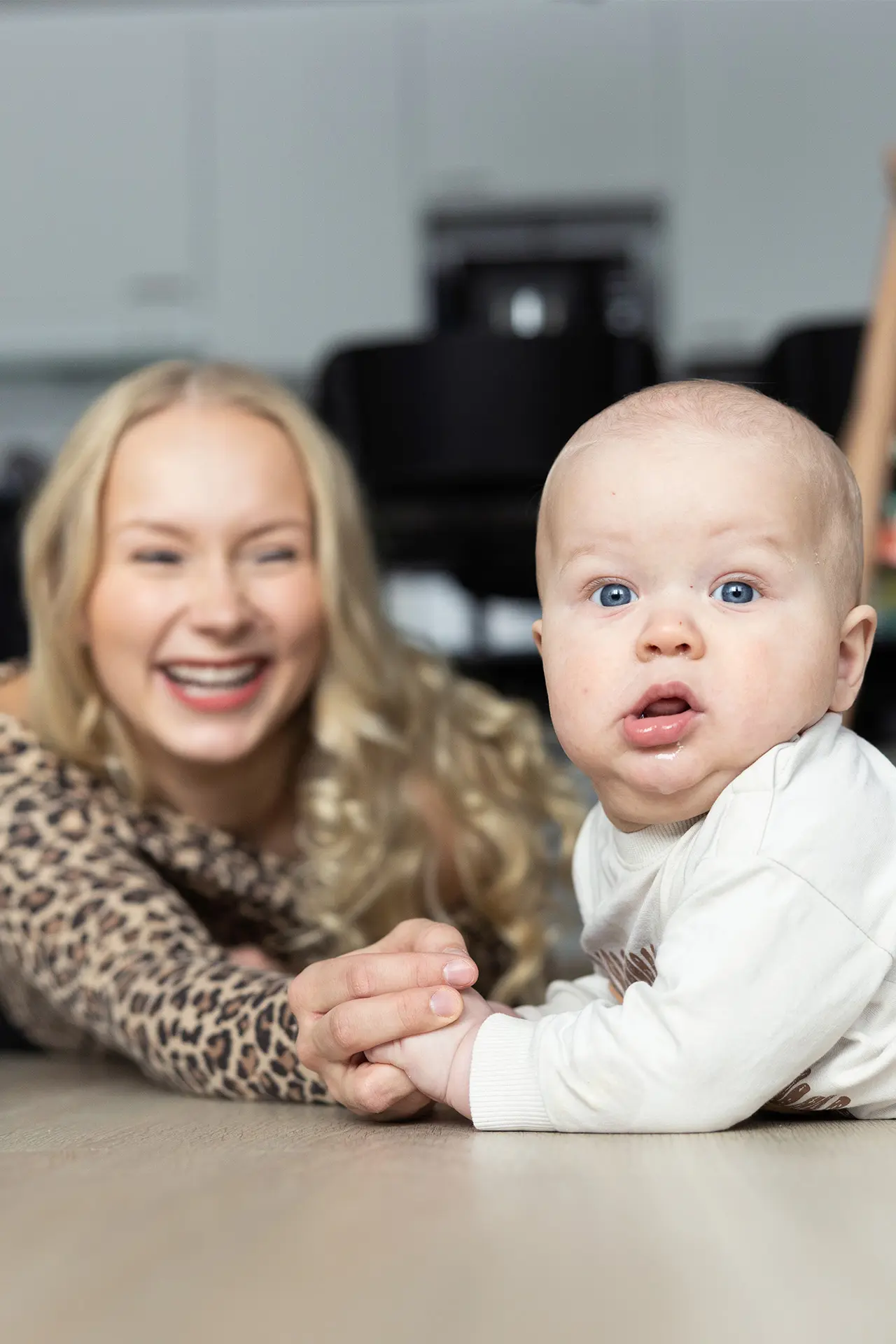 Äiti ja vauva makaavat lattialla ja katsovat kameraan