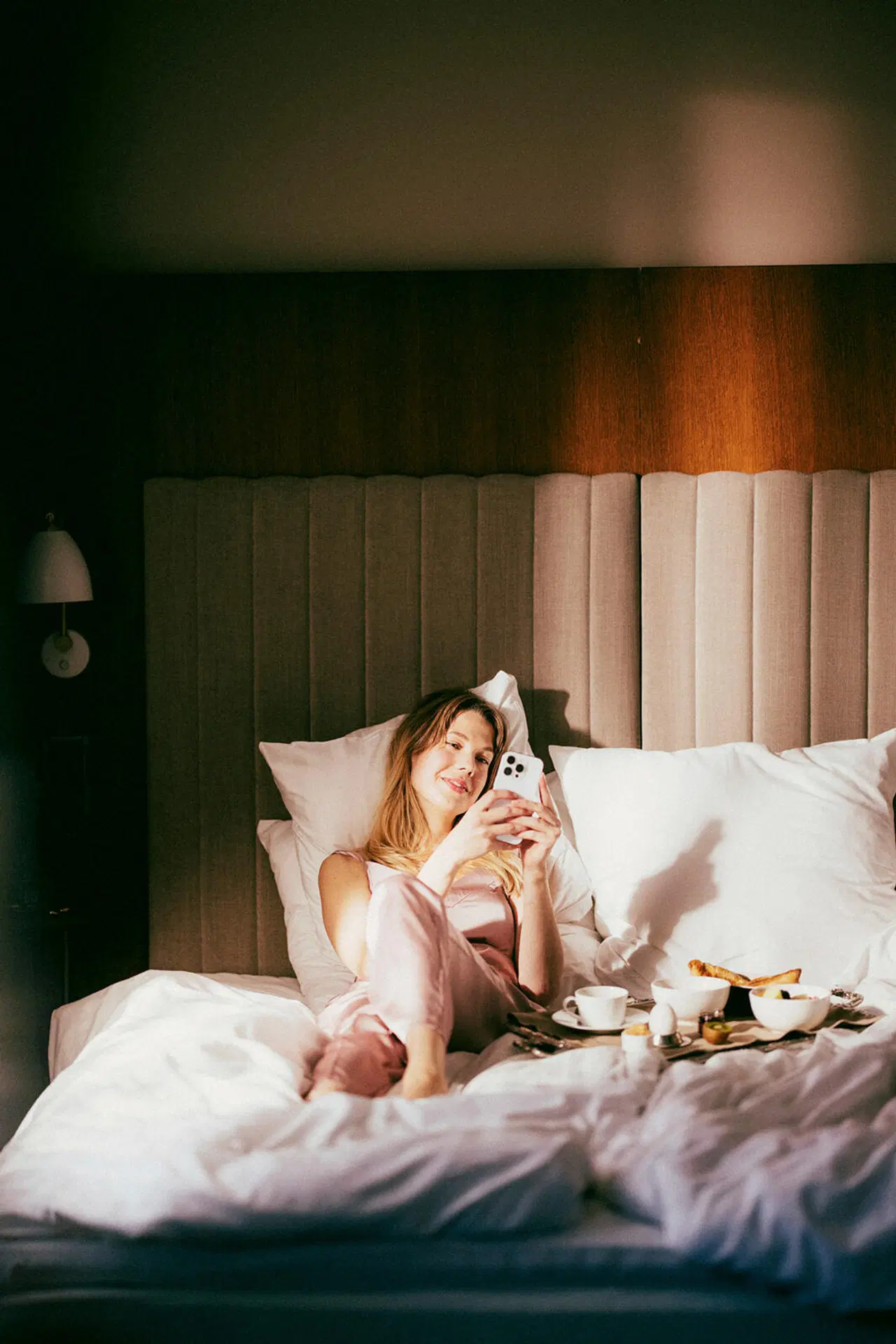 Nainen makaa hotellisängyssä ja selaa puhelinta.