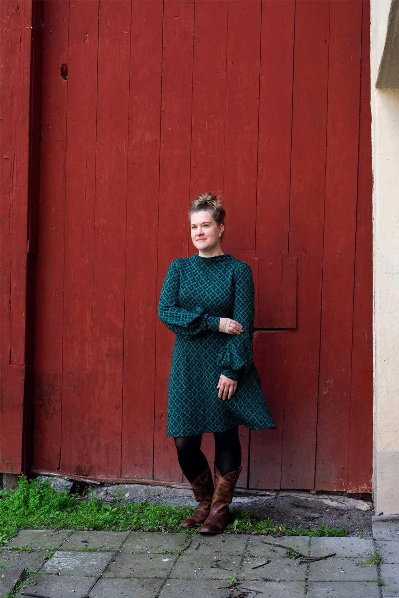 Tiina Kelanne poseeraa punaisen rakennuksen edessä