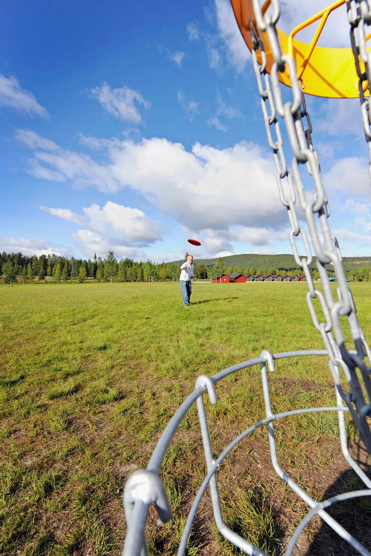 Henkilö heittää frisbeetä kohti frisbeegolfkoria.