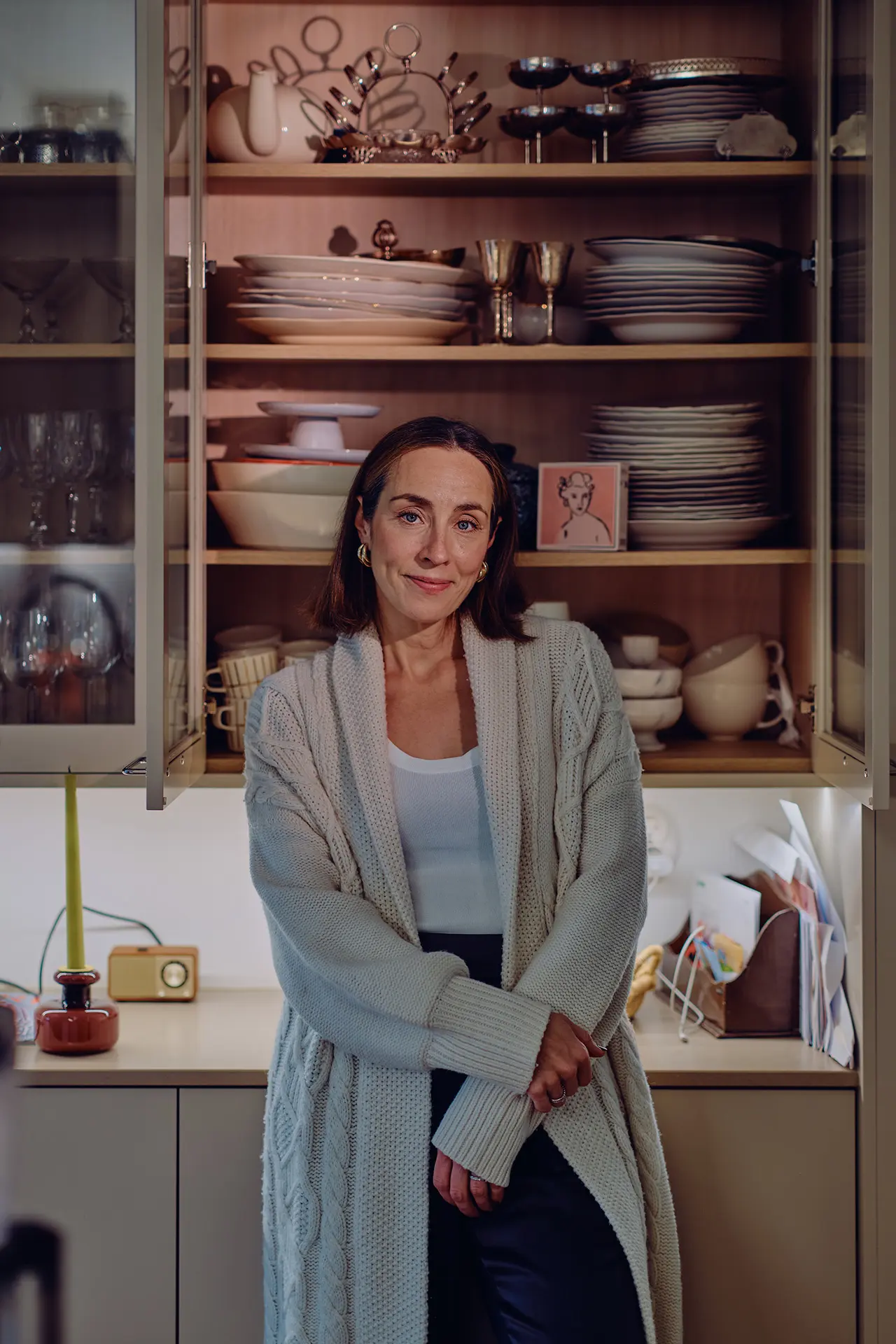 Anni Ihamäki keittiössä, takana näkyy aukinainen kaappi, joka on täynnä astioita