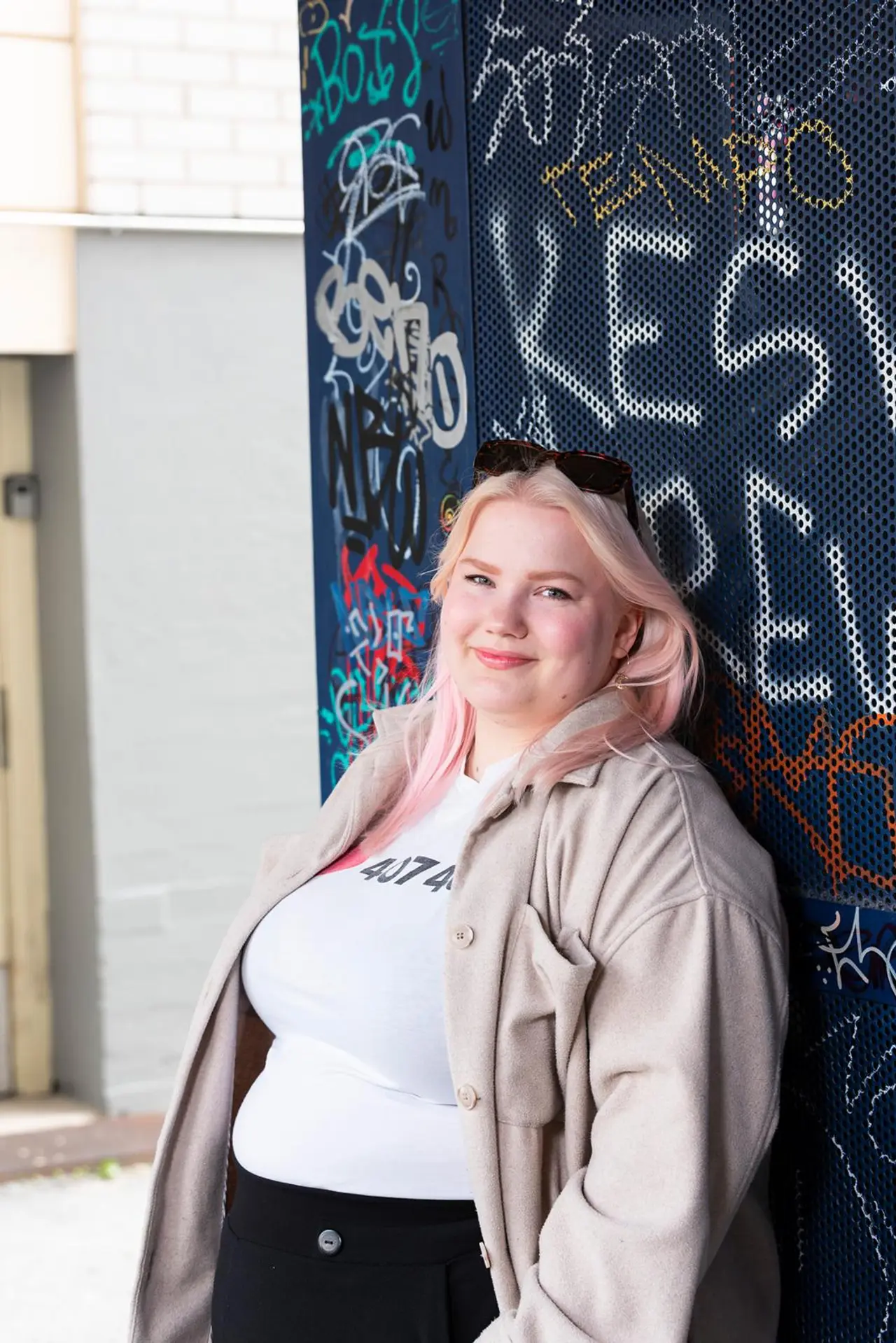 Amanda Mäkinen nojaa seinään, jossa on kirjoituksia.