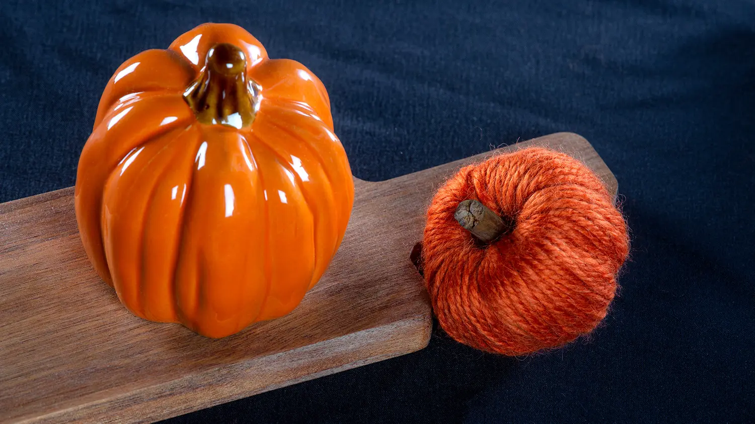 Langasta askarreltu koristekurpitsa, jonka vieressä on keraaminen koristekurpitsa puisen leikkuulaudan päällä.