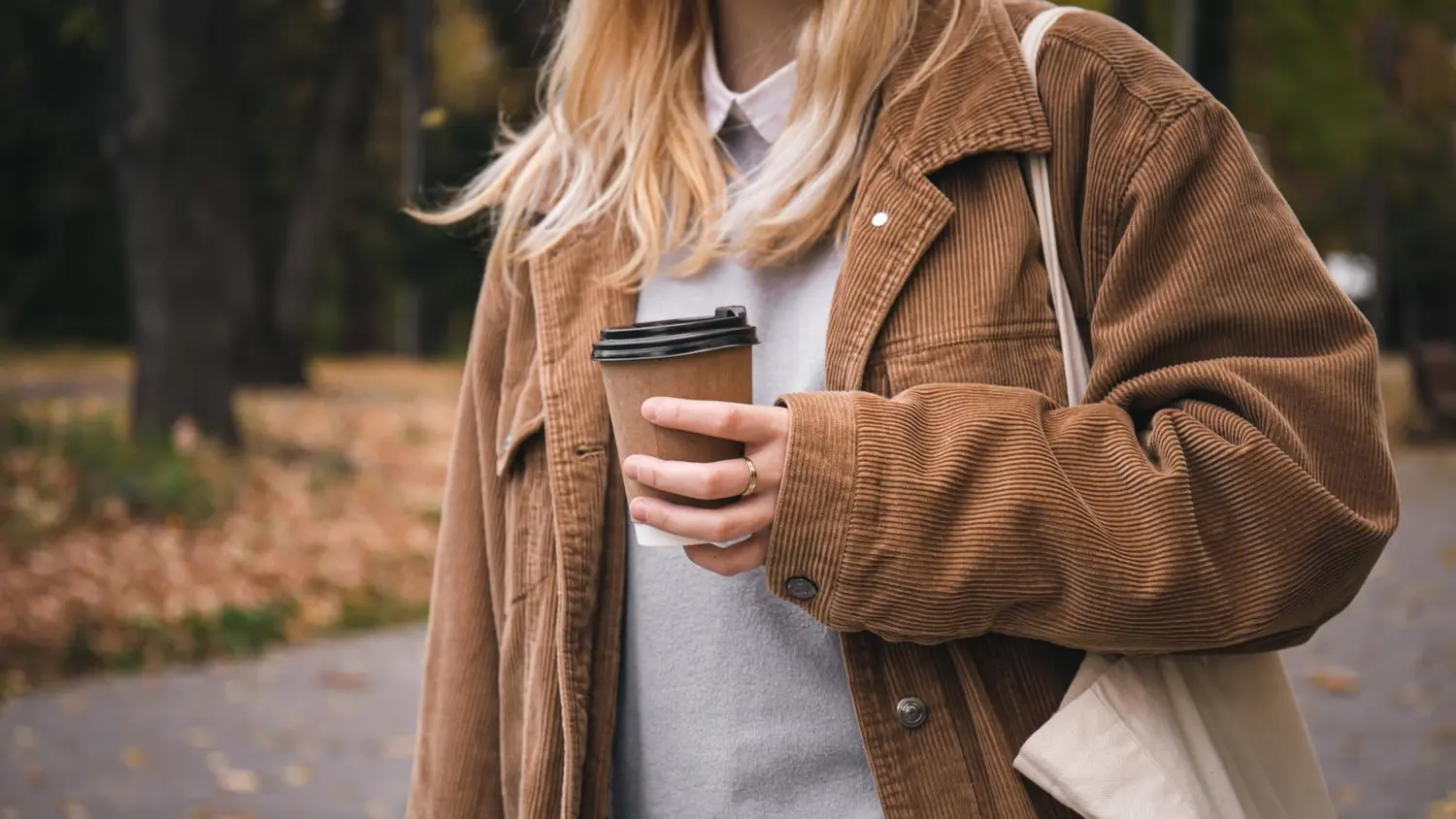 Vaaleaan vakosamettitakkiin pukeutunut nainen, jolla on kädessä take-away-kuppi