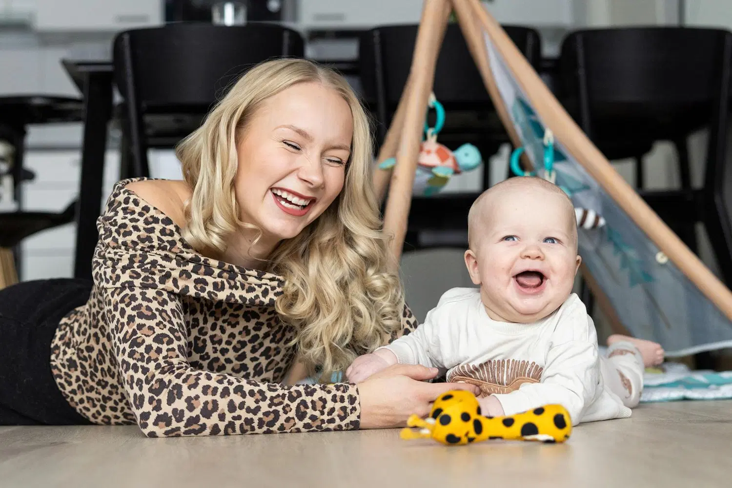 Äiti ja lapsi makaavat lattialla ja nauravat