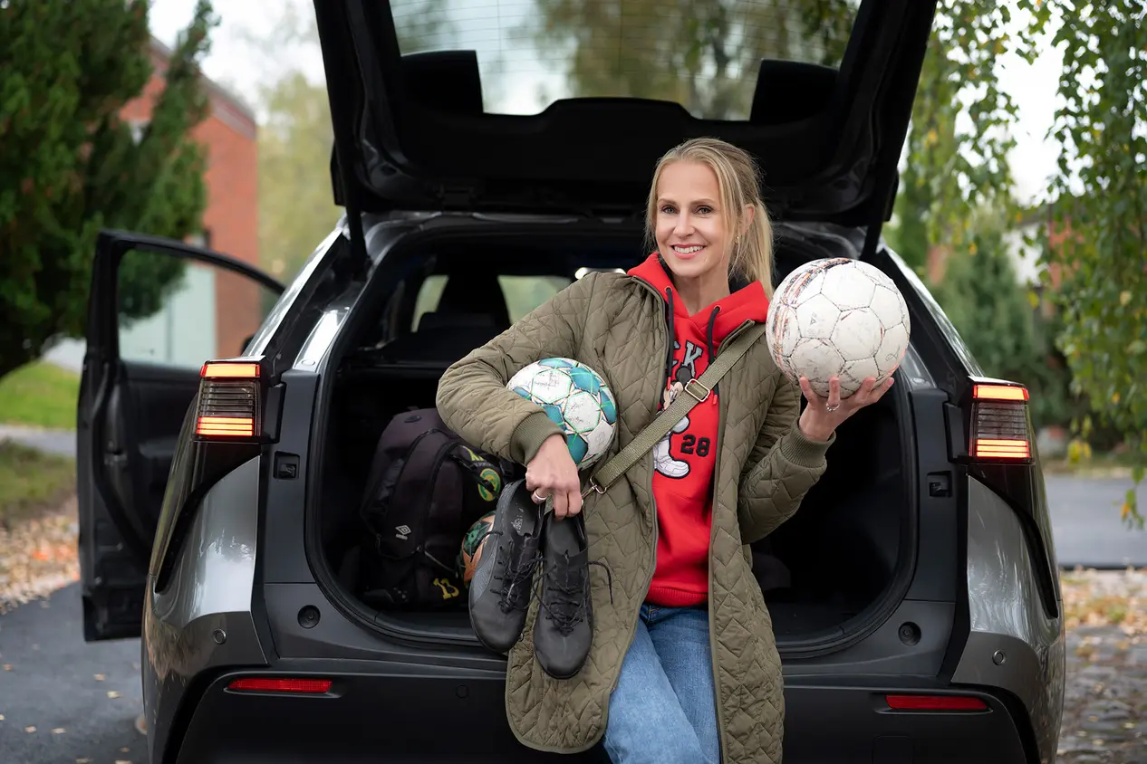 Joanna Kuvaja auton edessä, kädessään jalkapalloja ja jalkapallokengät