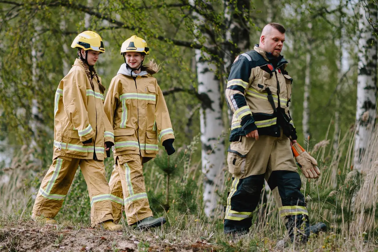 Eeva Kosonen, Sofia Lempiäinen ja Pasi Lappalainen kävelevät metsässä suojavarusteissa.