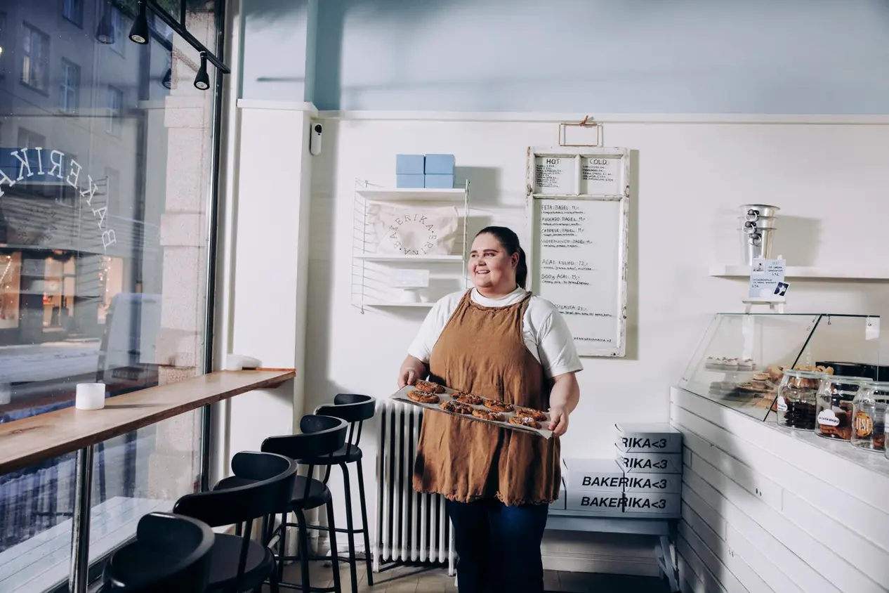 Erika Poussa seisoo kahvilassa pellillinen keksejä käsissään.