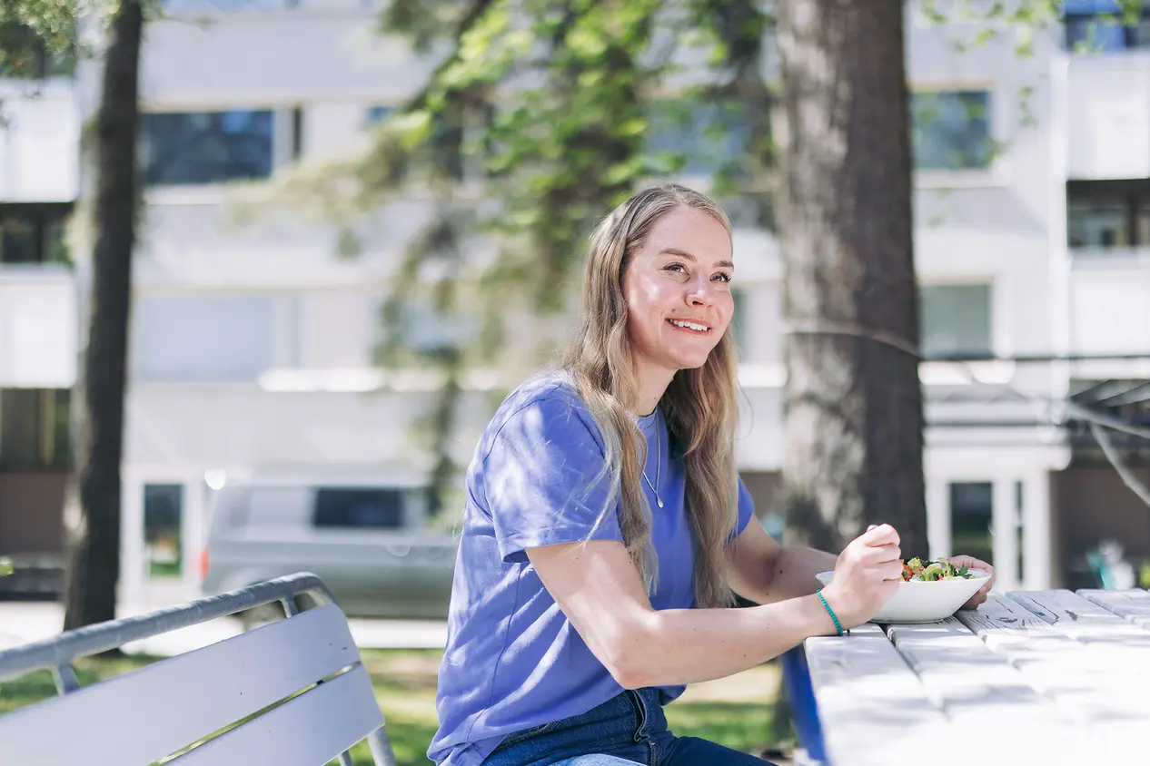Anni Penttilä syö salaattia kerrostalon pihalla.