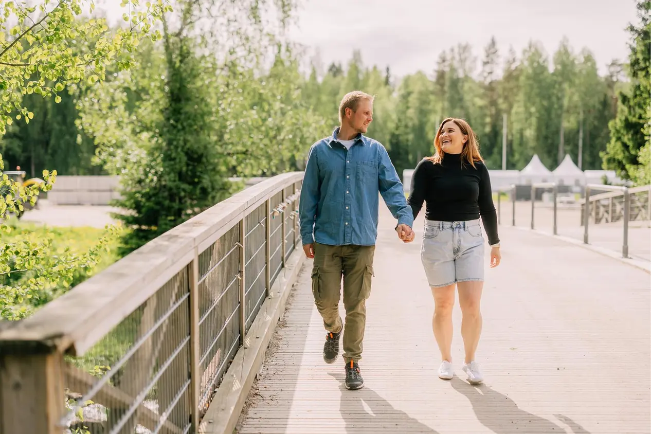 Mies ja nainen kävelevät käsi kädessä puusillalla