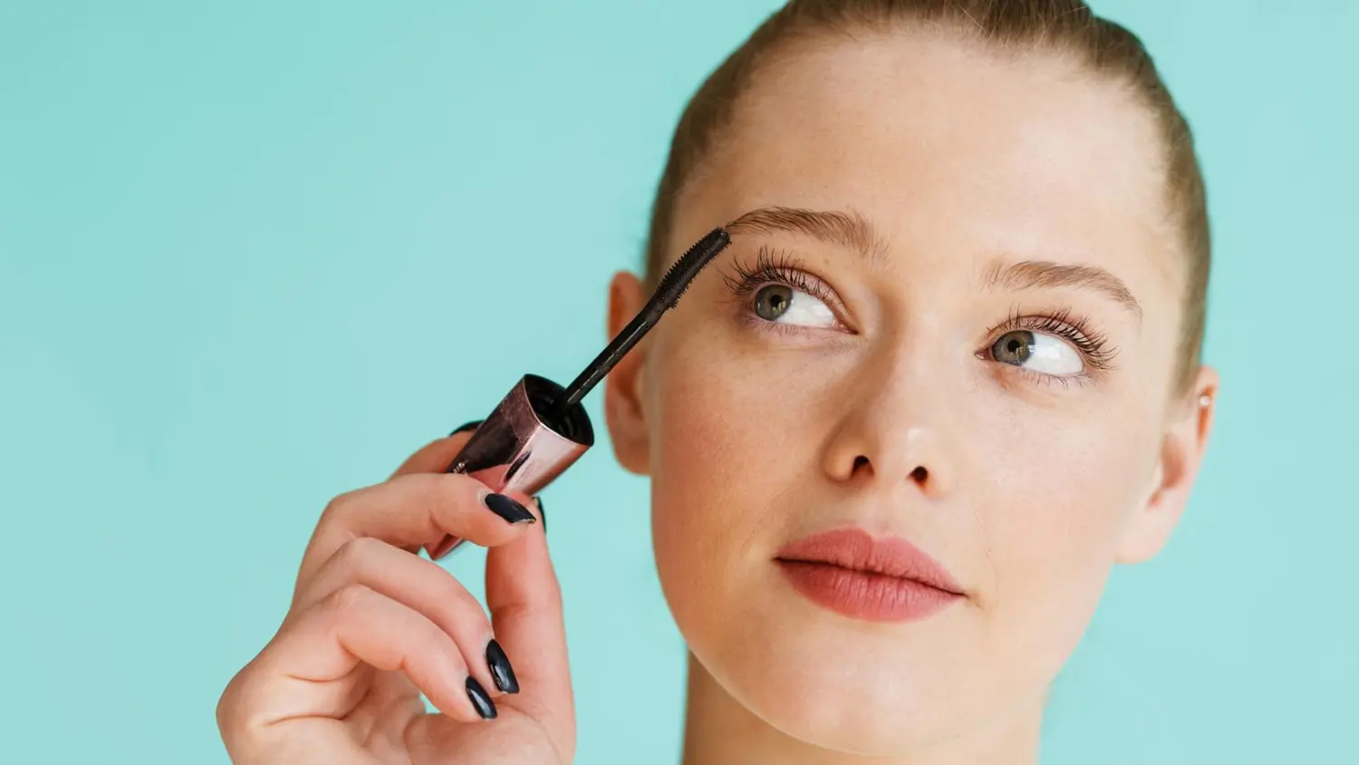 Ripsiväriä levittävä nainen vaaleanturkoosilla taustalla