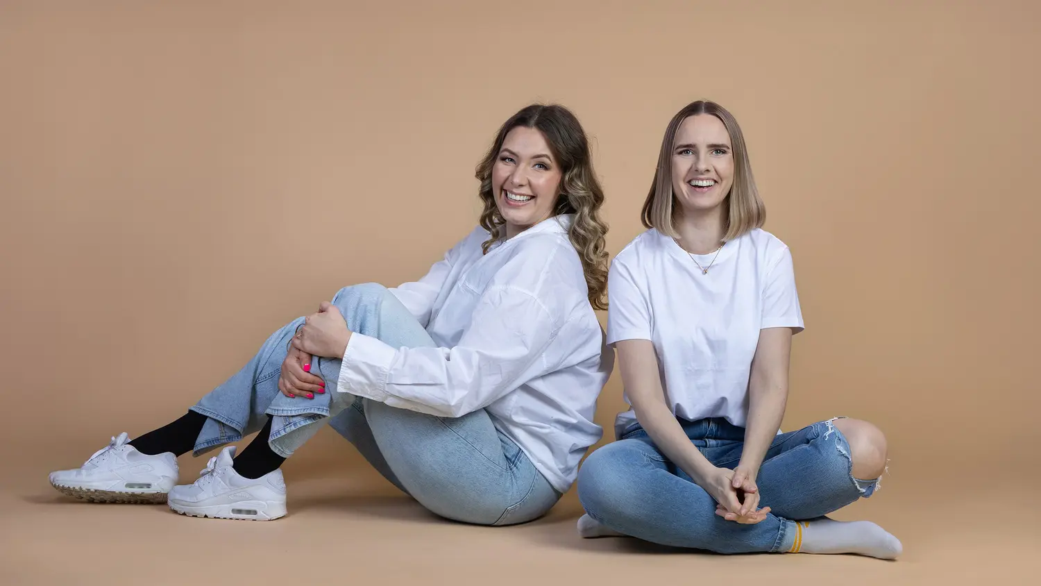 Kirjailijat Helena Rostedt ja Ronja Roms istuvat lattialla ja hymyilevät