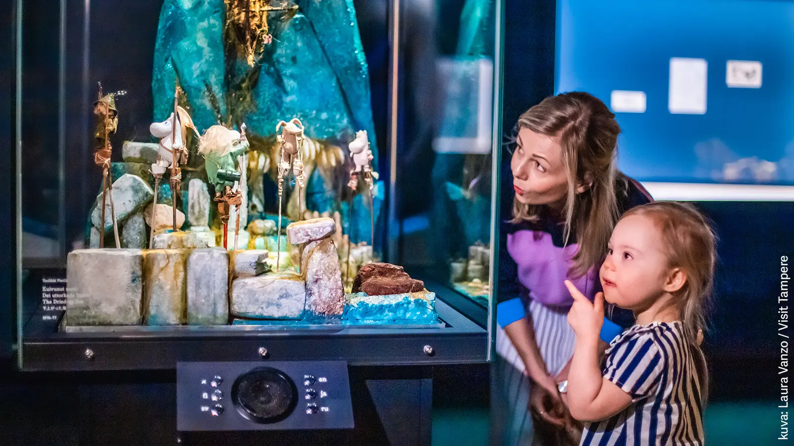 Lapsi ja aikuinen katselevat vitriinissä olevaa Muumiteosta Muumimuseossa.