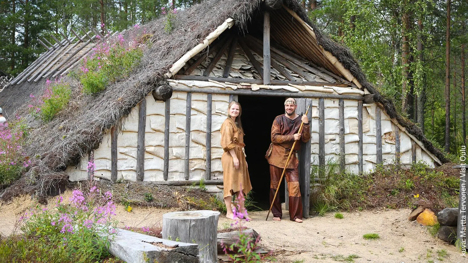 Kierikin museon kivikautinen rakennus ja kaksi työntekijää pukeutuneena sen ajan asuihin.