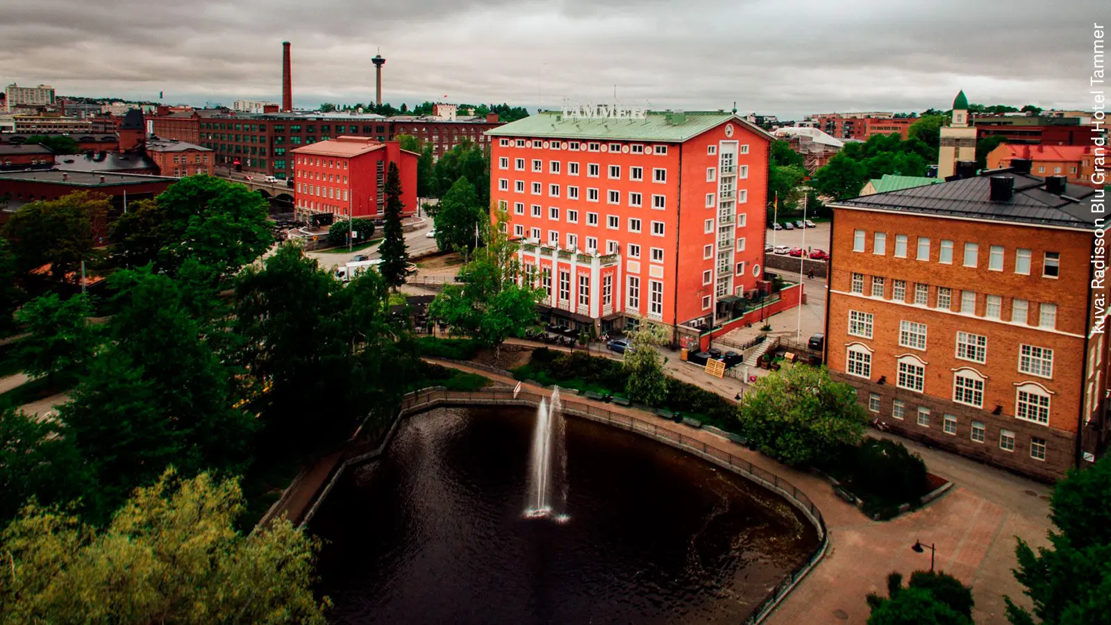 Punatiilisten tehdasrakennusten ympäröimä Radisson Blu Grand Hotel Tammer. Edustalla suihkulähde. 