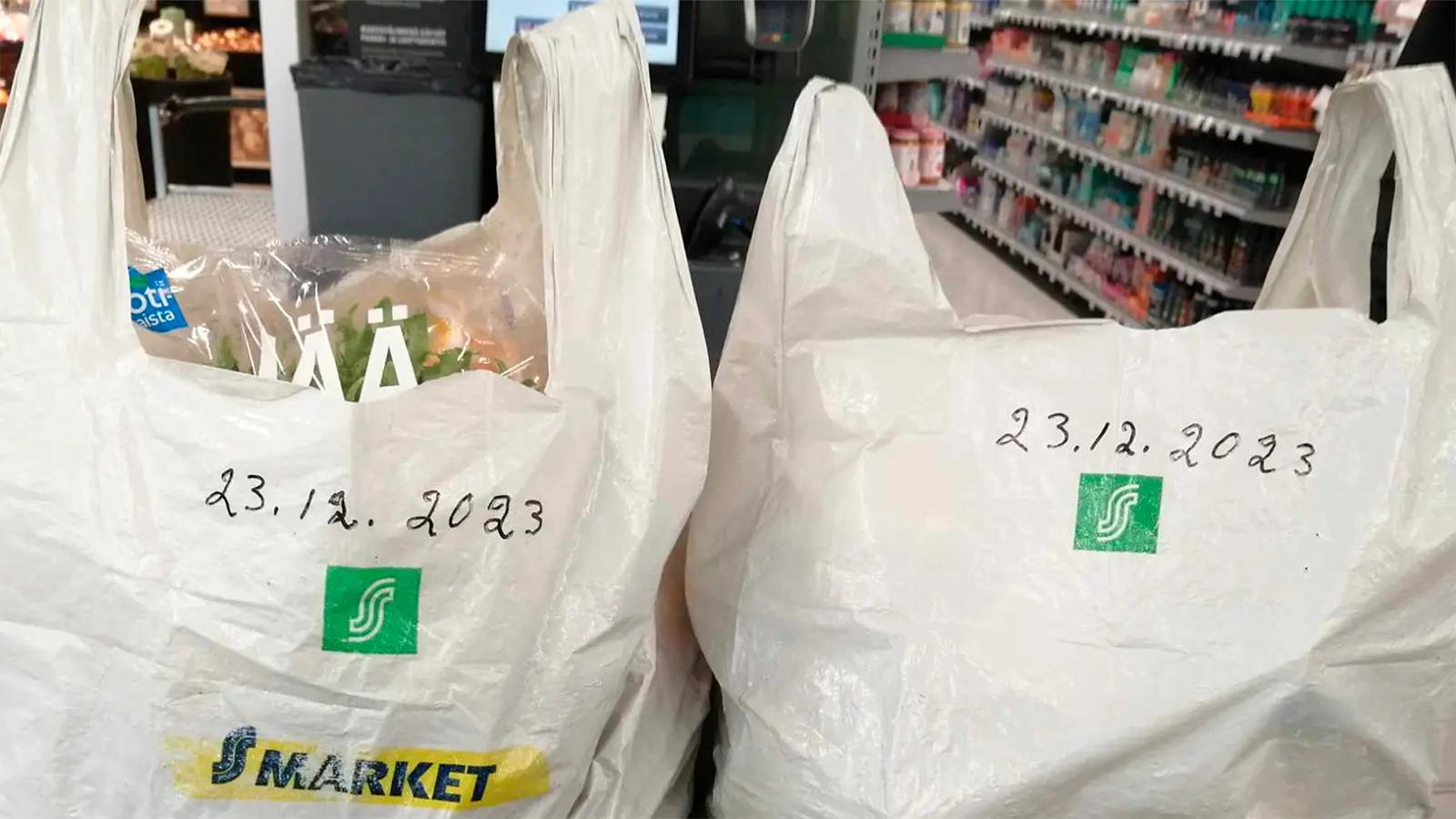 Kuvassa kaksi vanhaa S-marketin pussia täynnä ruokaa. Pusseihin kirjoitettu tussilla päivämäärät 23.12.2023