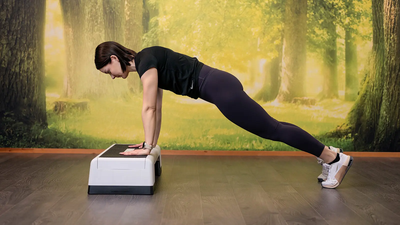 Nainen kädet suorina steppilaudalla, muuten lankkuasennossa.