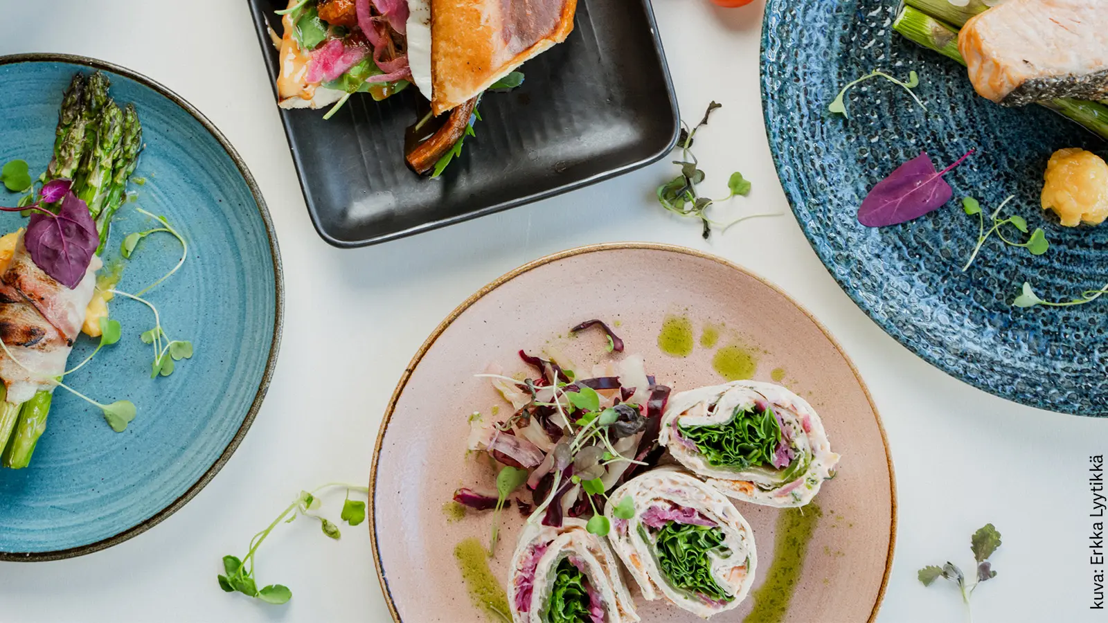 Erilaisia annoksia värikkäillä lautasilla ylhäältä kuvattuna.