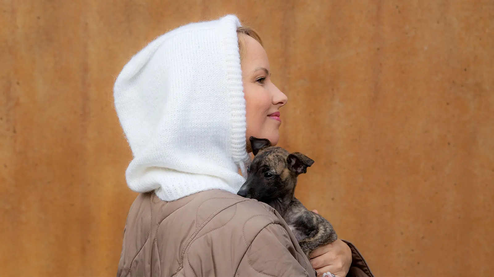 Sivusta päin kuvattu nainen, joka on pukeutunut balaclavaan ja jonka sylissä on pieni koira.