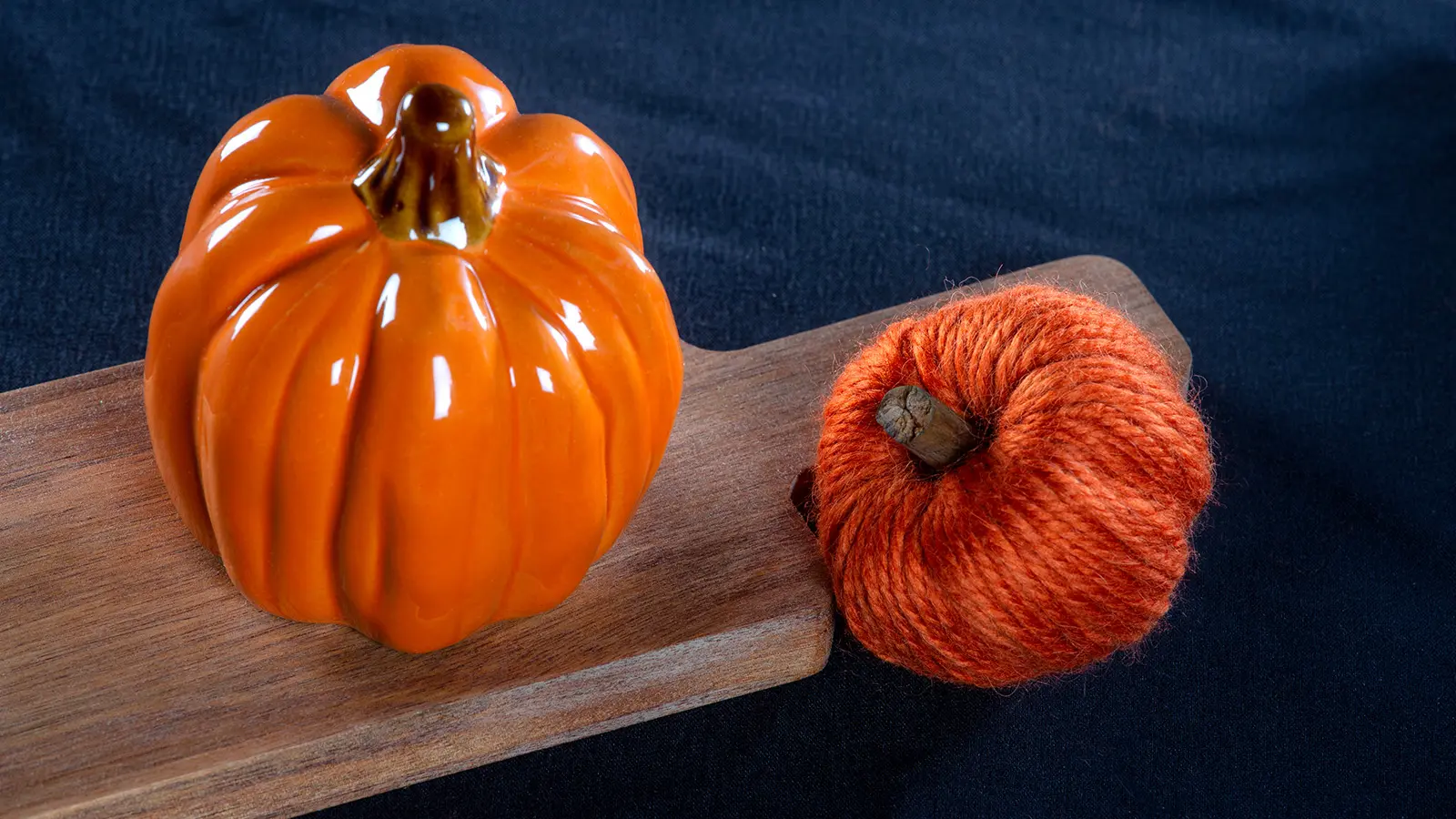 Langasta askarreltu koristekurpitsa, jonka vieressä on keraaminen koristekurpitsa puisen leikkuulaudan päällä.