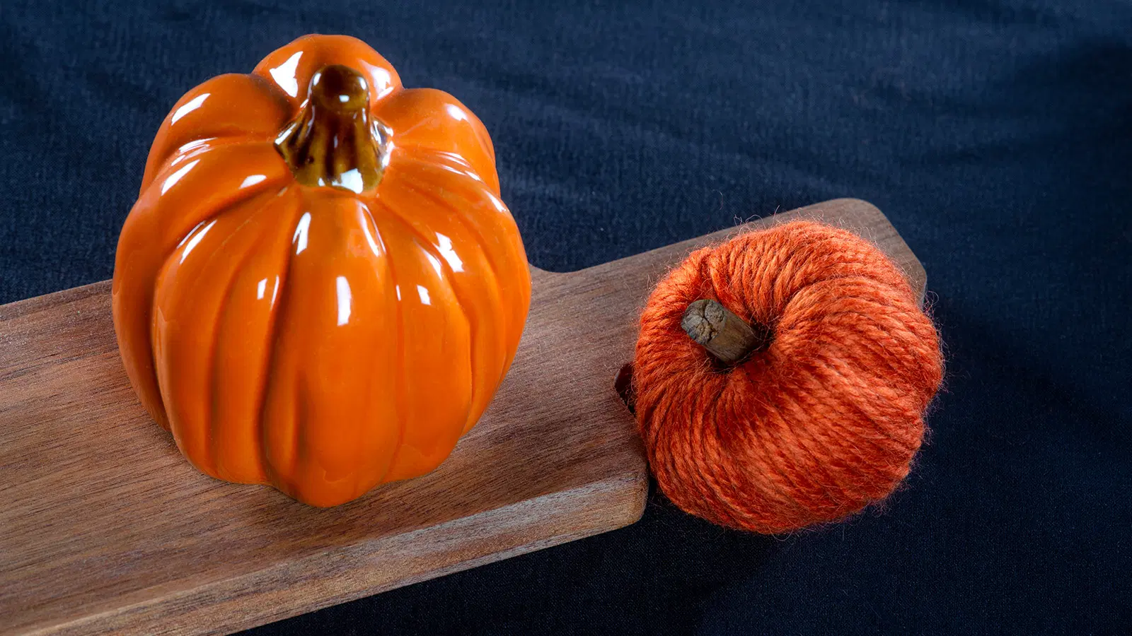 Langasta askarreltu koristekurpitsa, jonka vieressä on keraaminen koristekurpitsa puisen leikkuulaudan päällä.