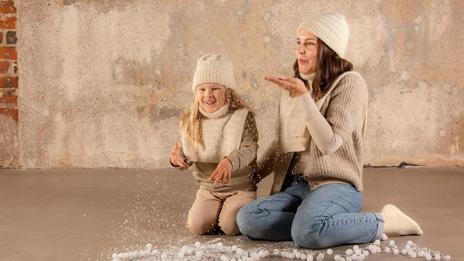 Pipoon ja kauluriin pukeutunut lapsi ja nainen istumassa lattialla.