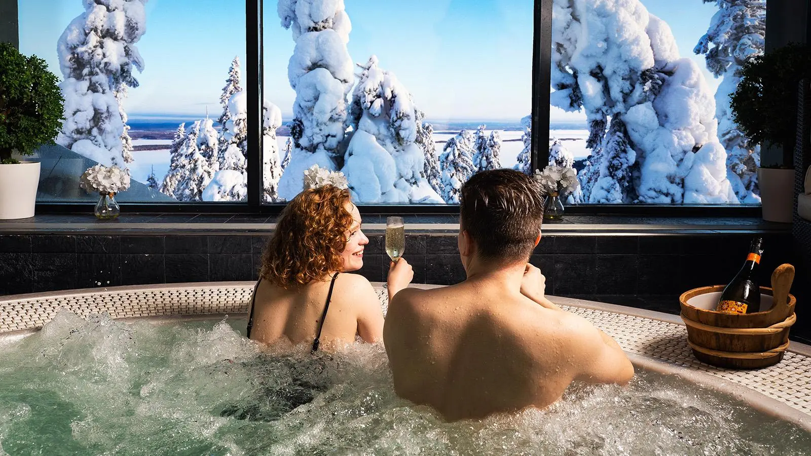 Nainen ja mies poreltaassa ikkunan edessä, ikkunan takana luminen maisema