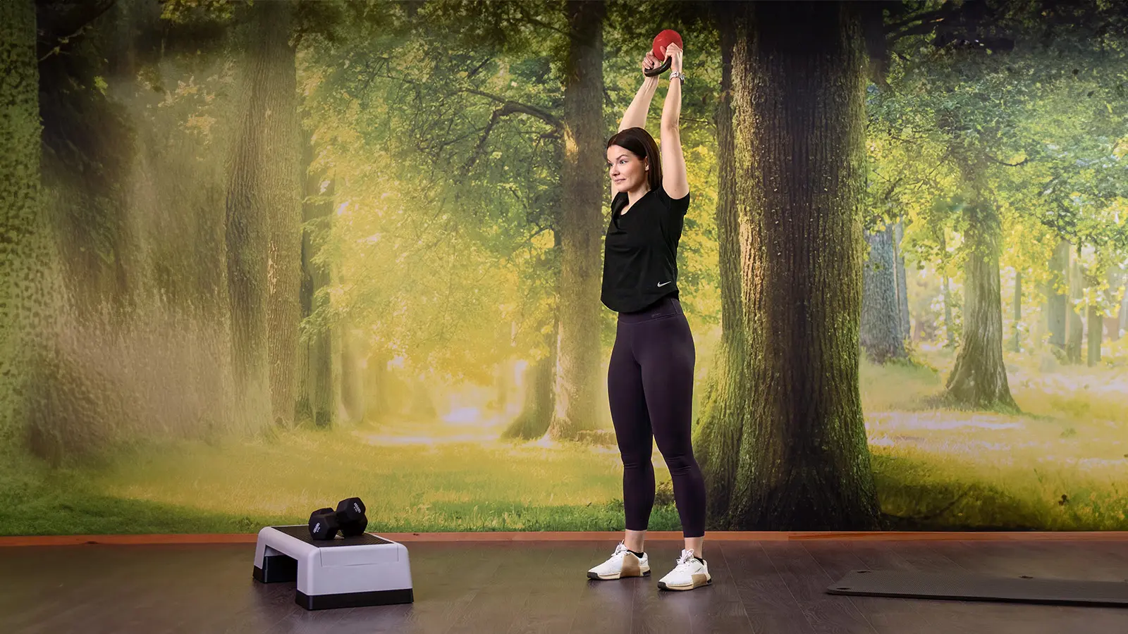 Nainen on nostanut kahvakuulan päänsä yläpuolelle.