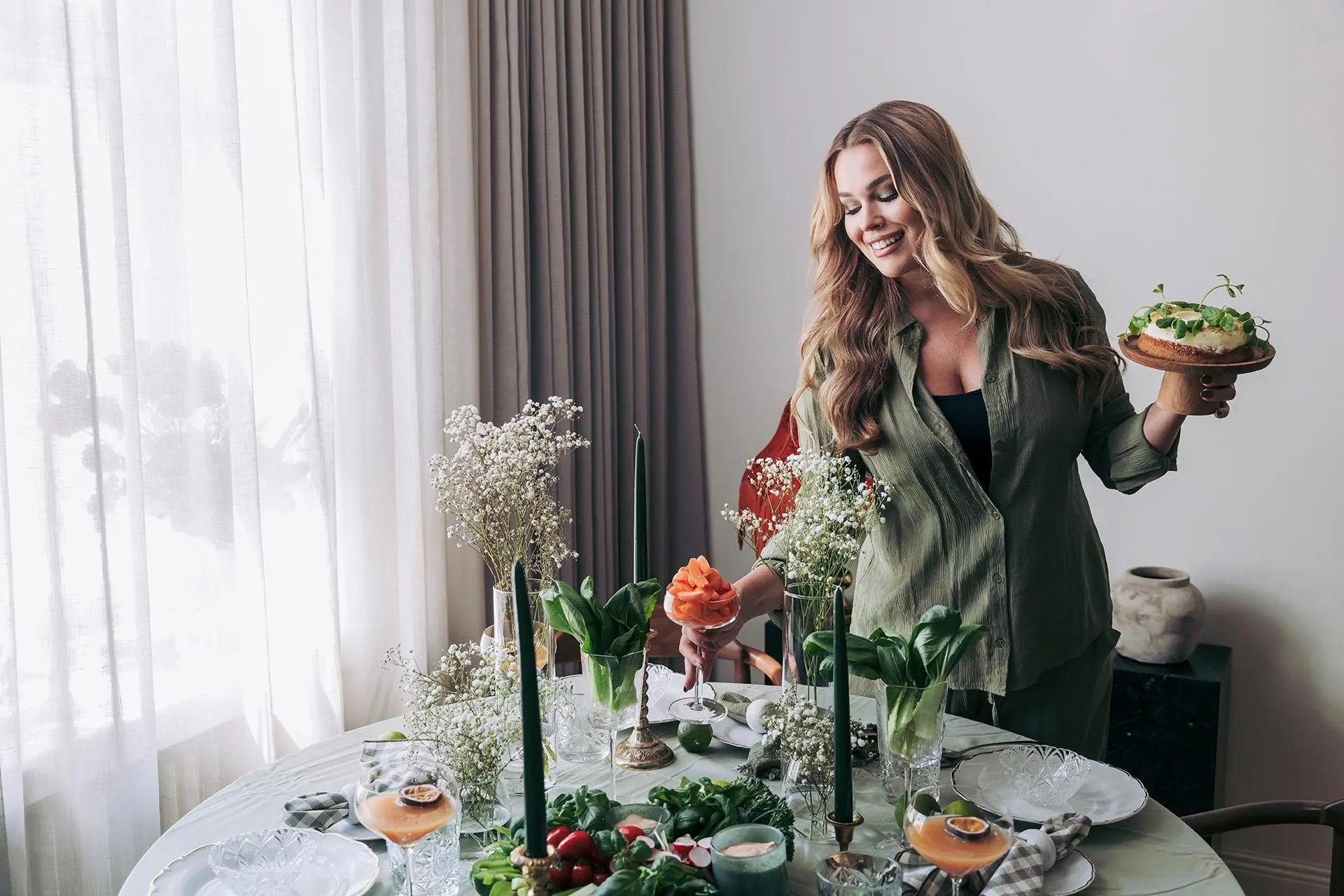 Sara Sieppi seisoo kauniisti katetun pöydän vieressä ja pitää kädessään mintunlehdillä koristeltua kakkua.