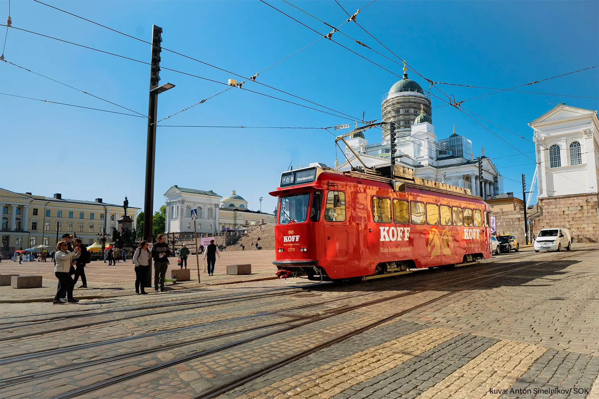 Punainen Koff-ratikka ajaa kesäisessä säässä Senaatintorin edustalla.