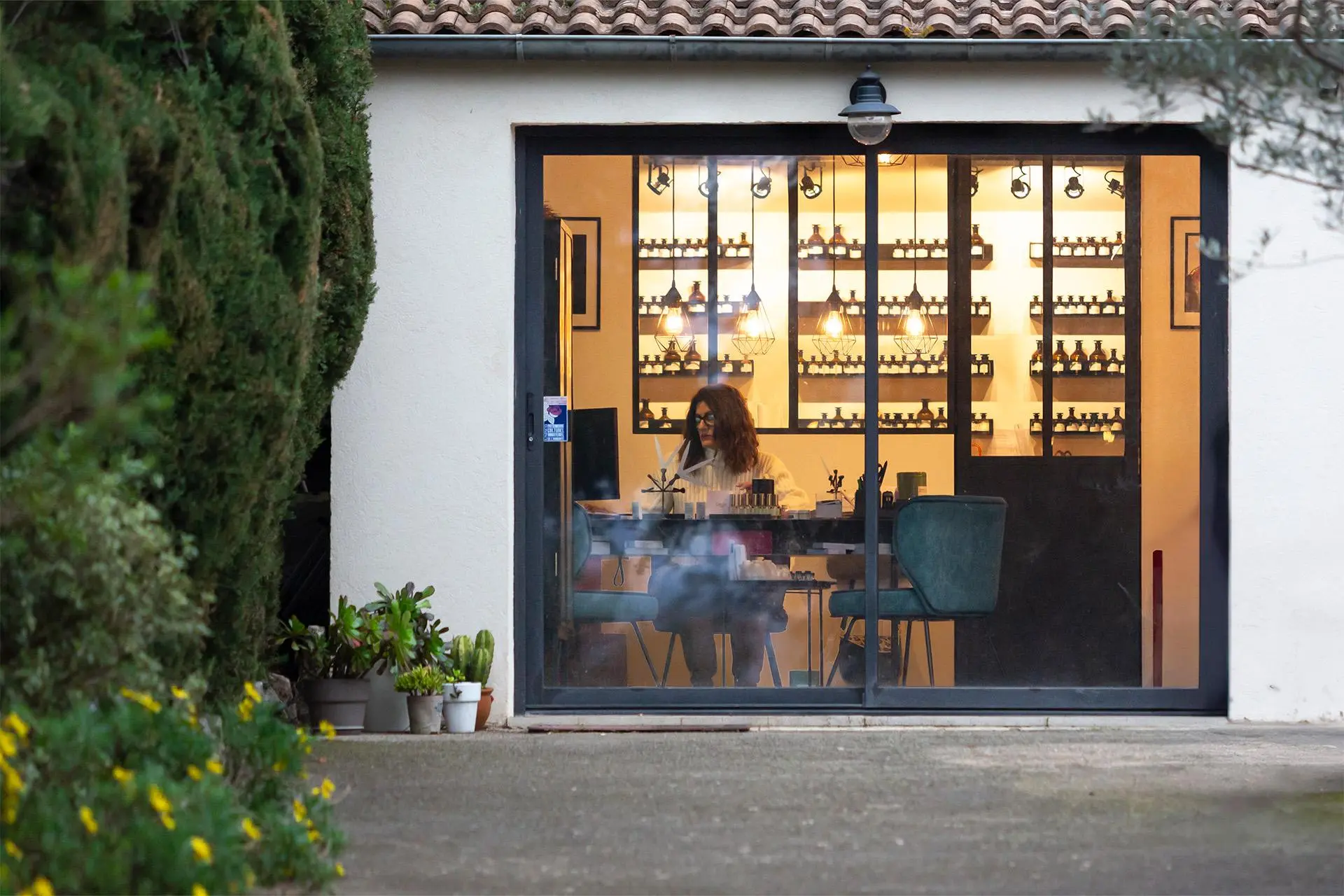 Joëlle Lerioux Patris istuu työpöydän ääressä talossa, jonka hyllyillä on pieniä lasipurkkeja.