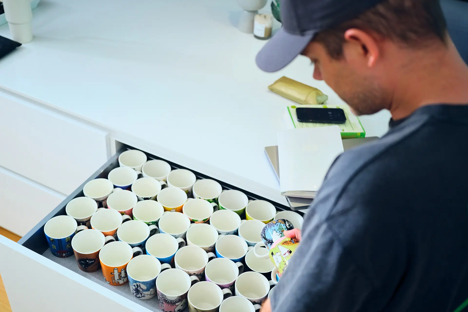 Niko Saarinen katselee muumimukeja, jotka täyttävät aukinaisen vetolaatikon. Mukit ovat siisteissä riveissä.