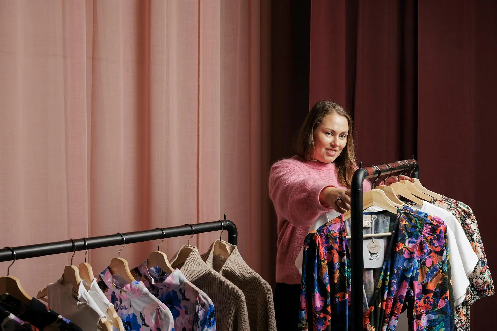 Vaatebrändi Kaikon perustaja Mirjam Sokka katselee rekillä olevia värikkäitä vaatteita.