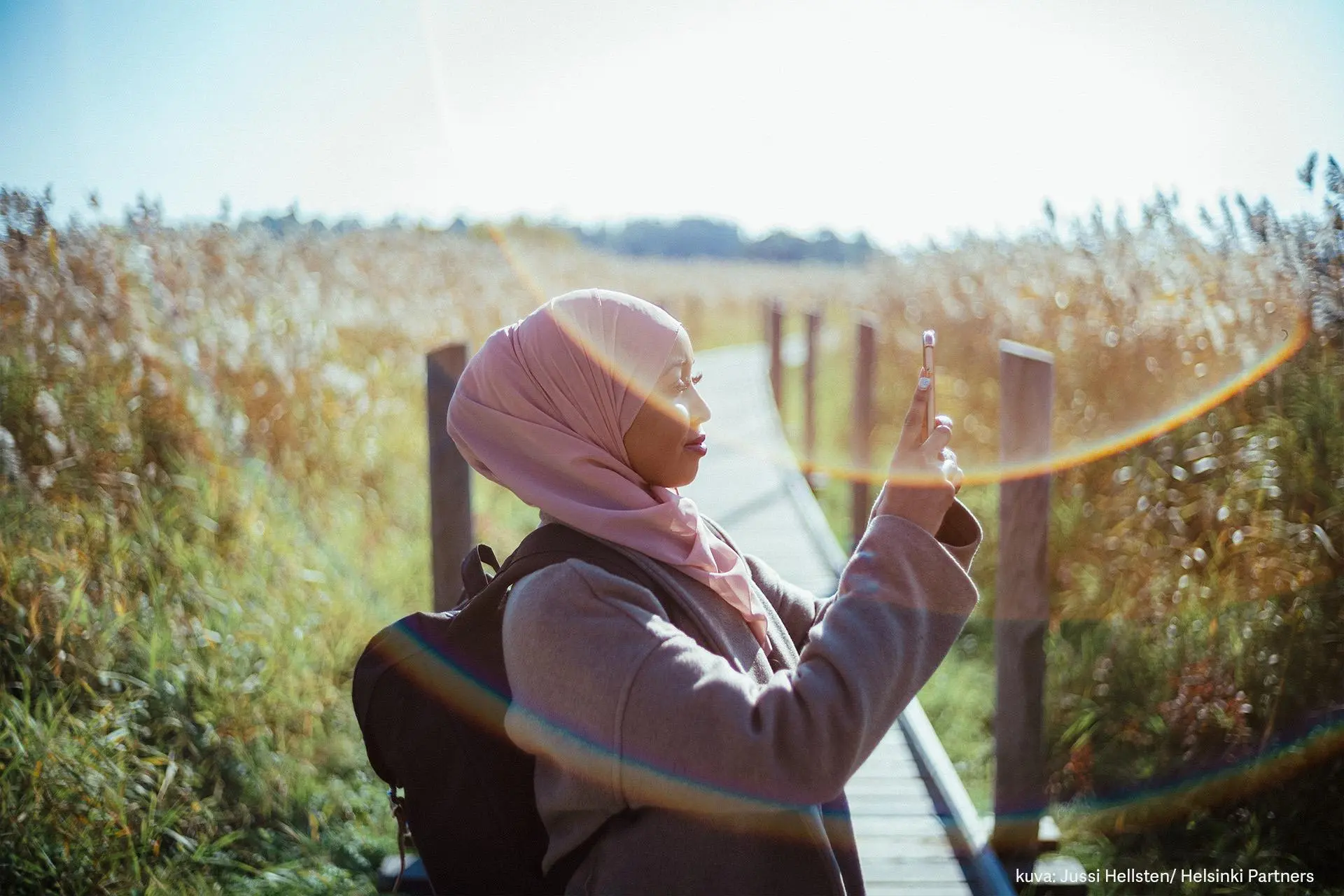 Nuori nainen ottaa kuvaa Lammassaaren pitkospuilla kaislikon keskellä.