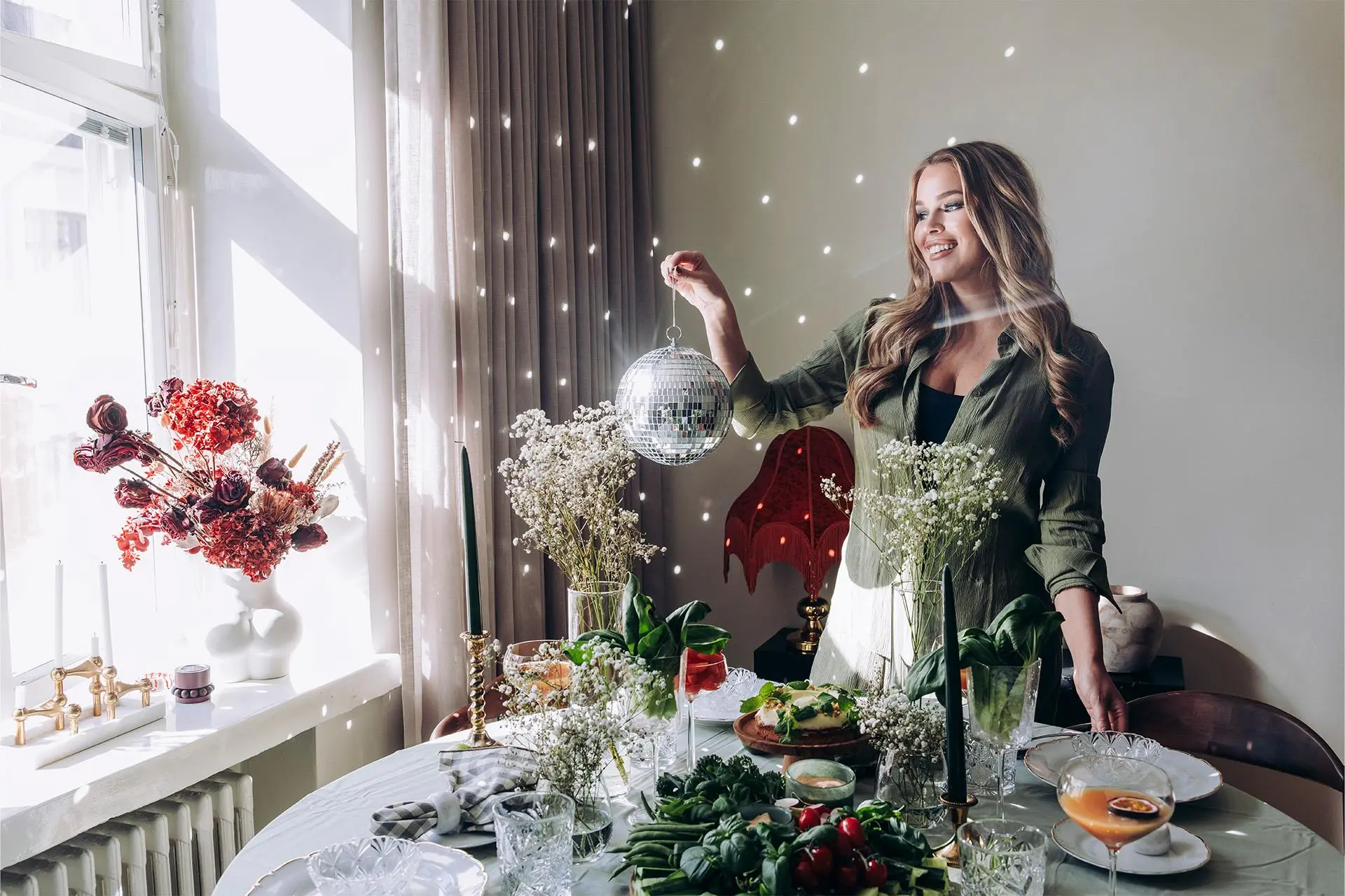 Sara Sieppi seisoo kauniisti katetun pöydän ääressä ja pitää kädessään peilipalloa.