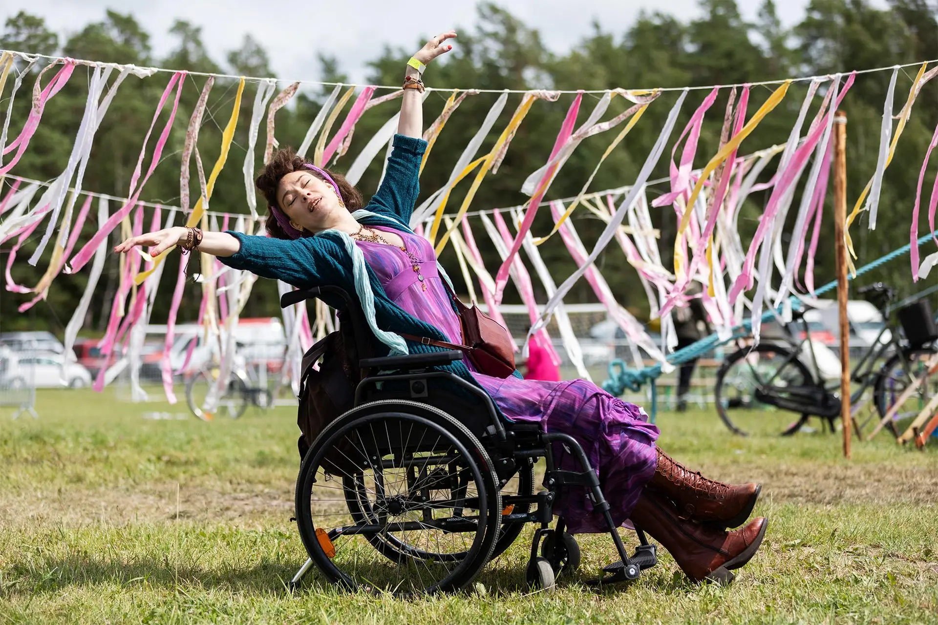 Kirsi Ylinen istuu pyörätuolissa ulkona paikassa, joka on koristeltu viirinauhoin.