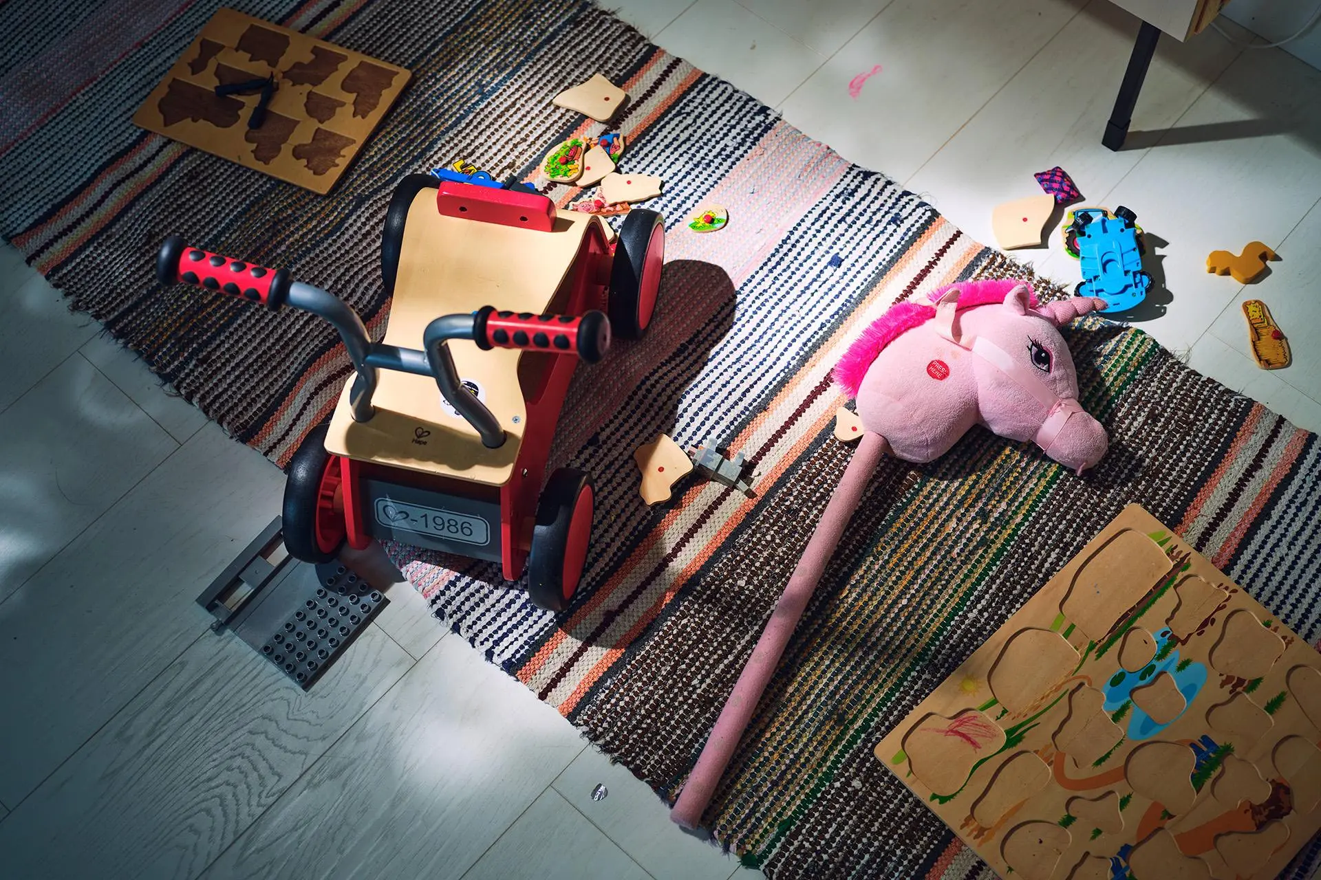 Leluja lattialla: potkuauto, keppihevonen ja palapeleä.