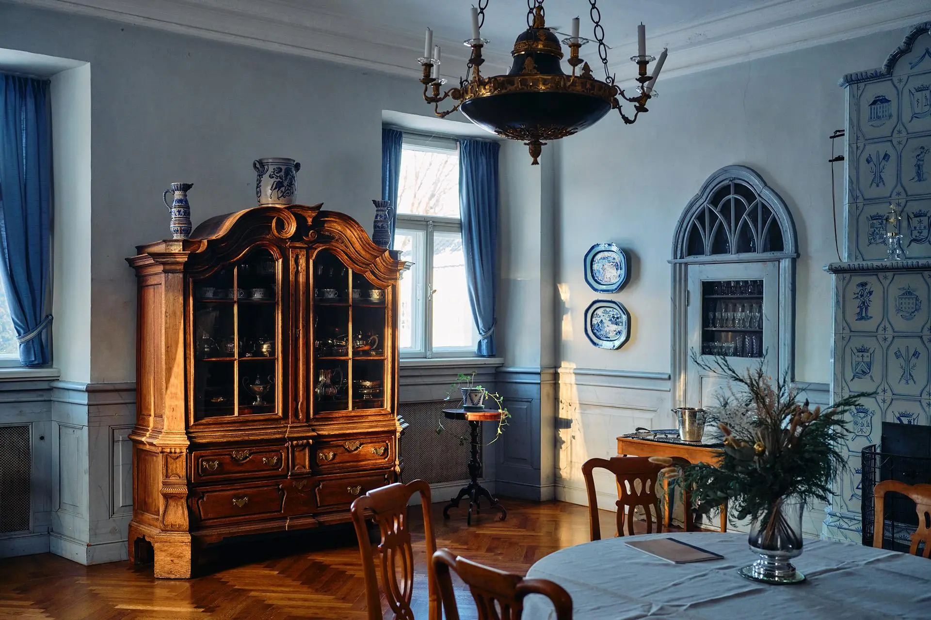 Huone, jossa on ruokapöytä, kakluuni, kaappi ja kaksi ikkunaa.