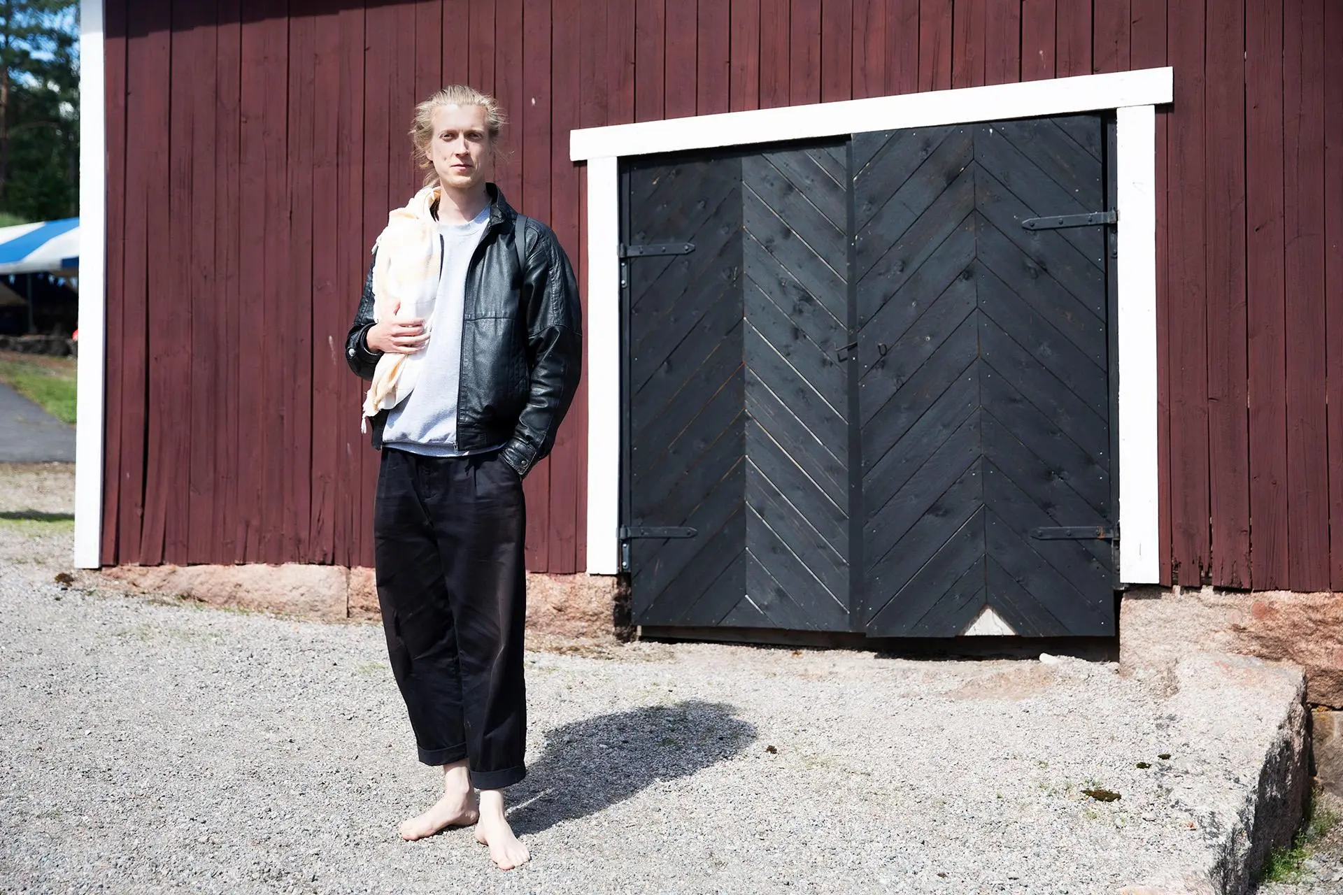 Karri Rasinmäki seisoo nahkatakki ja housut yllään puisen rakennuksen edessä.