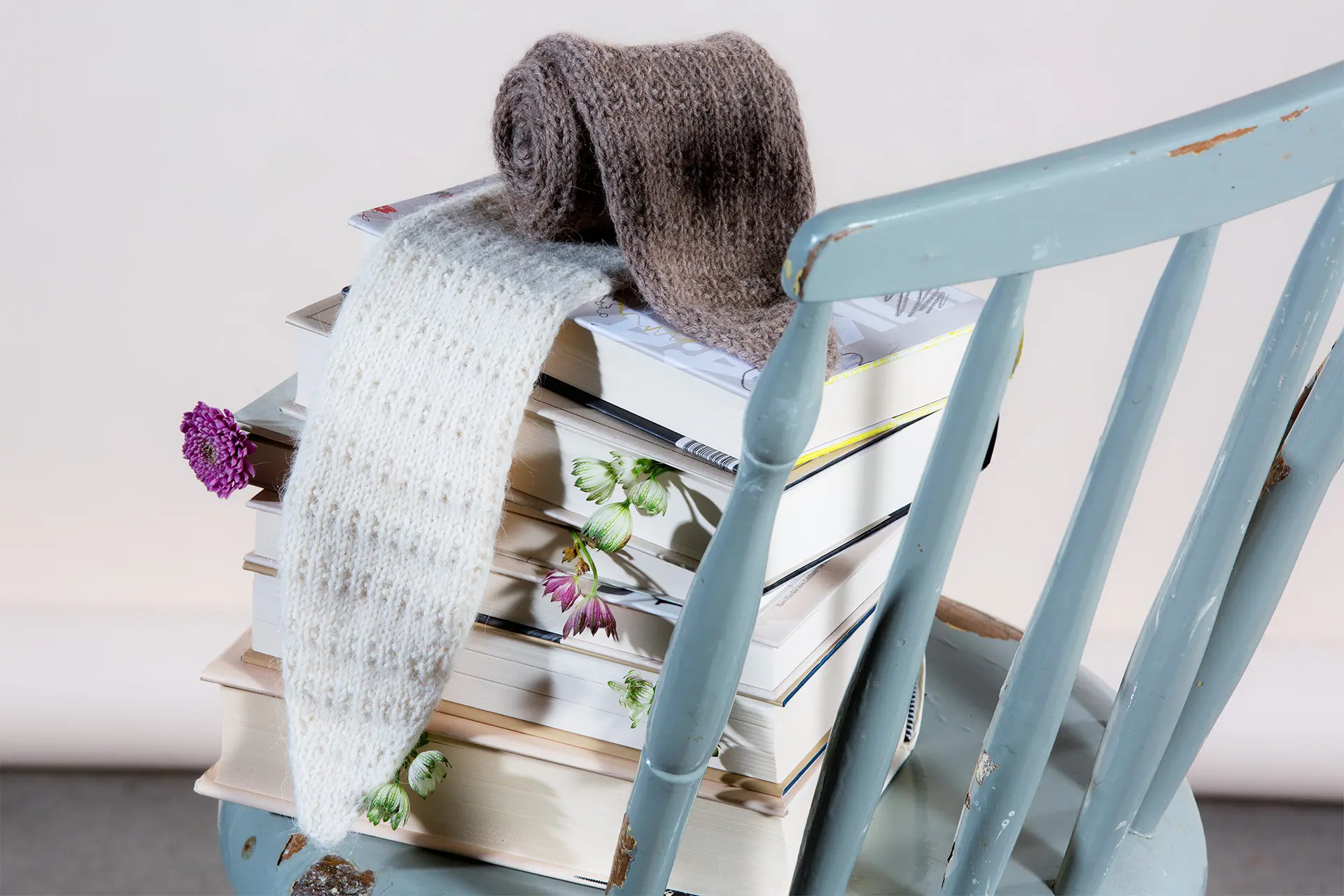 Valkoinen ja ruskea pieni neulehuivi tuolilla olevan kirjapinon päällä.