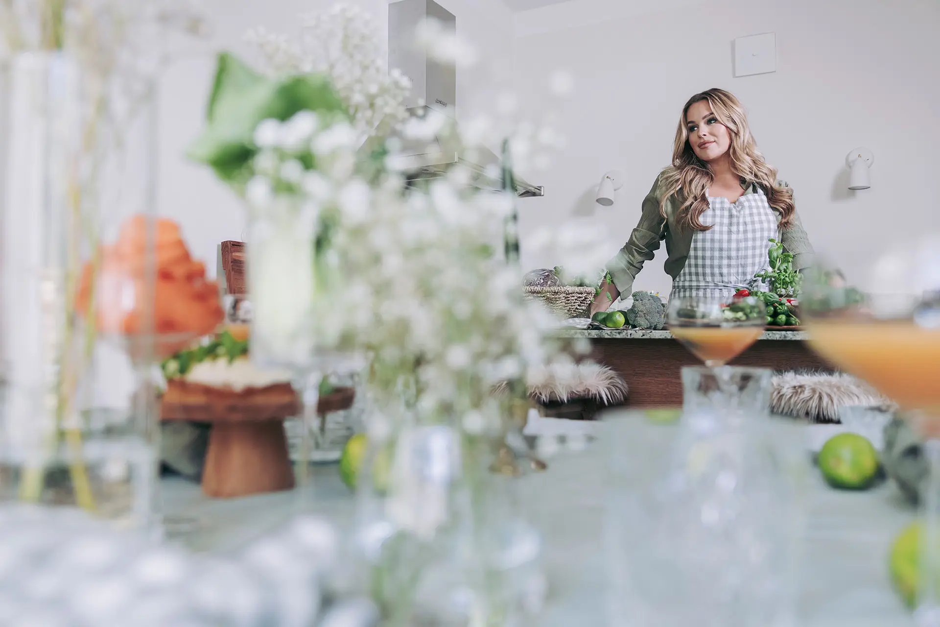 Sara Sieppi keittiössä ruudullinen esiliina päällä. Etualalla katettu pöytä