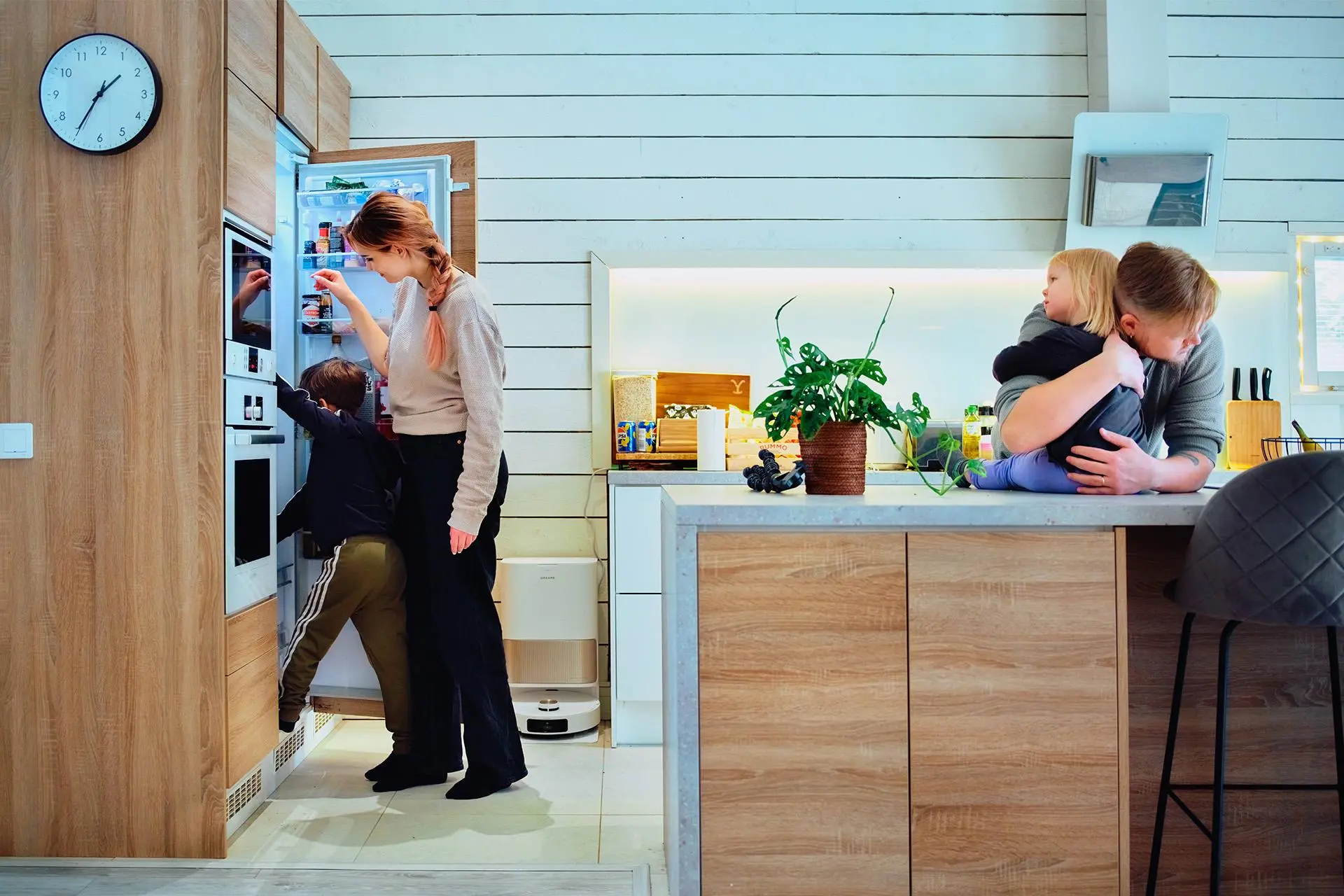 Maria Kangskortet ja lapsi kurkistavat jääkappiin. Tommi Kangaskortet halaa keittiön tasolla istuvaa lasta.