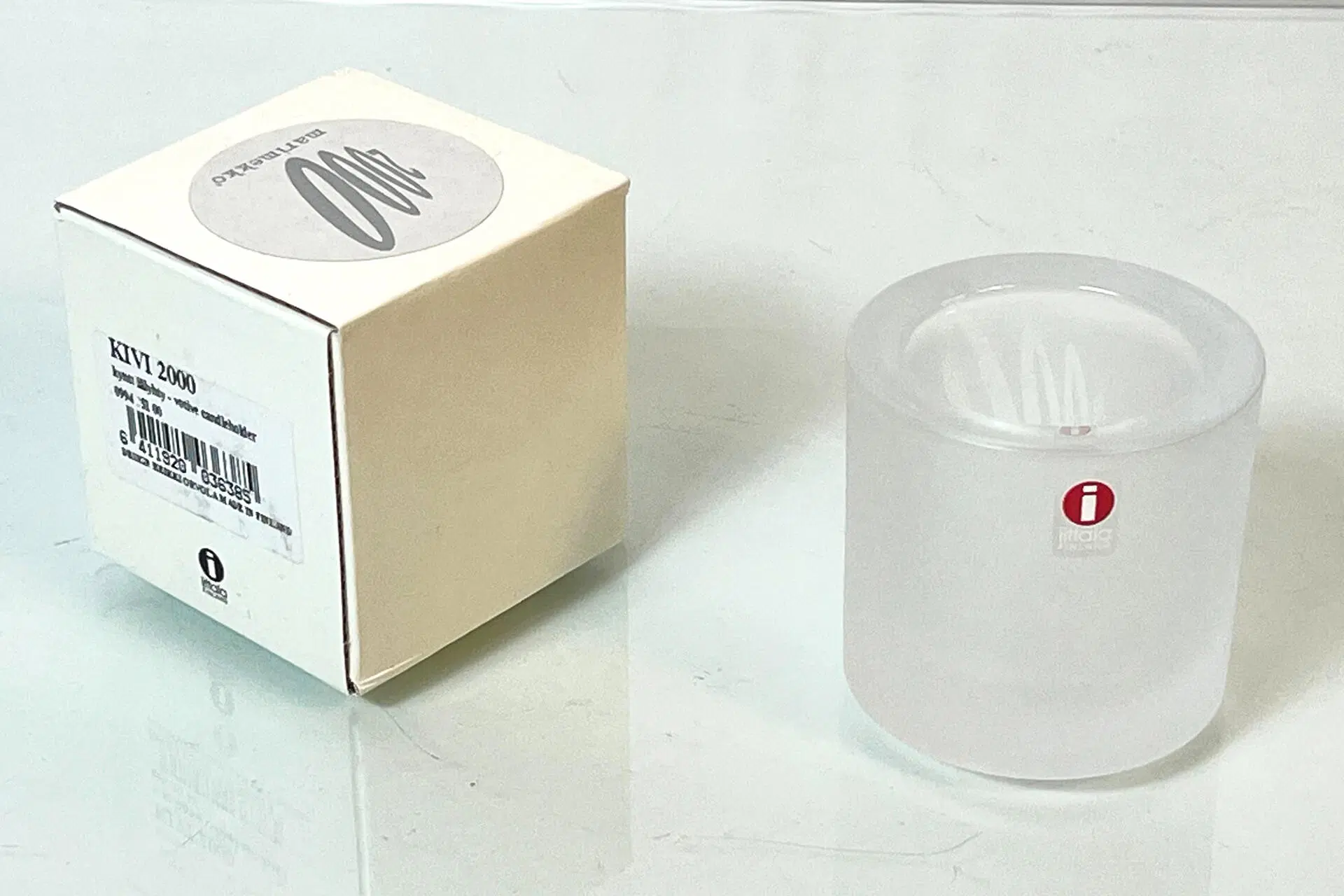 Kirkas Iittala Kivi-kynttilälyhty ja sen valkoinen laatikko valkoisella pinnalla.