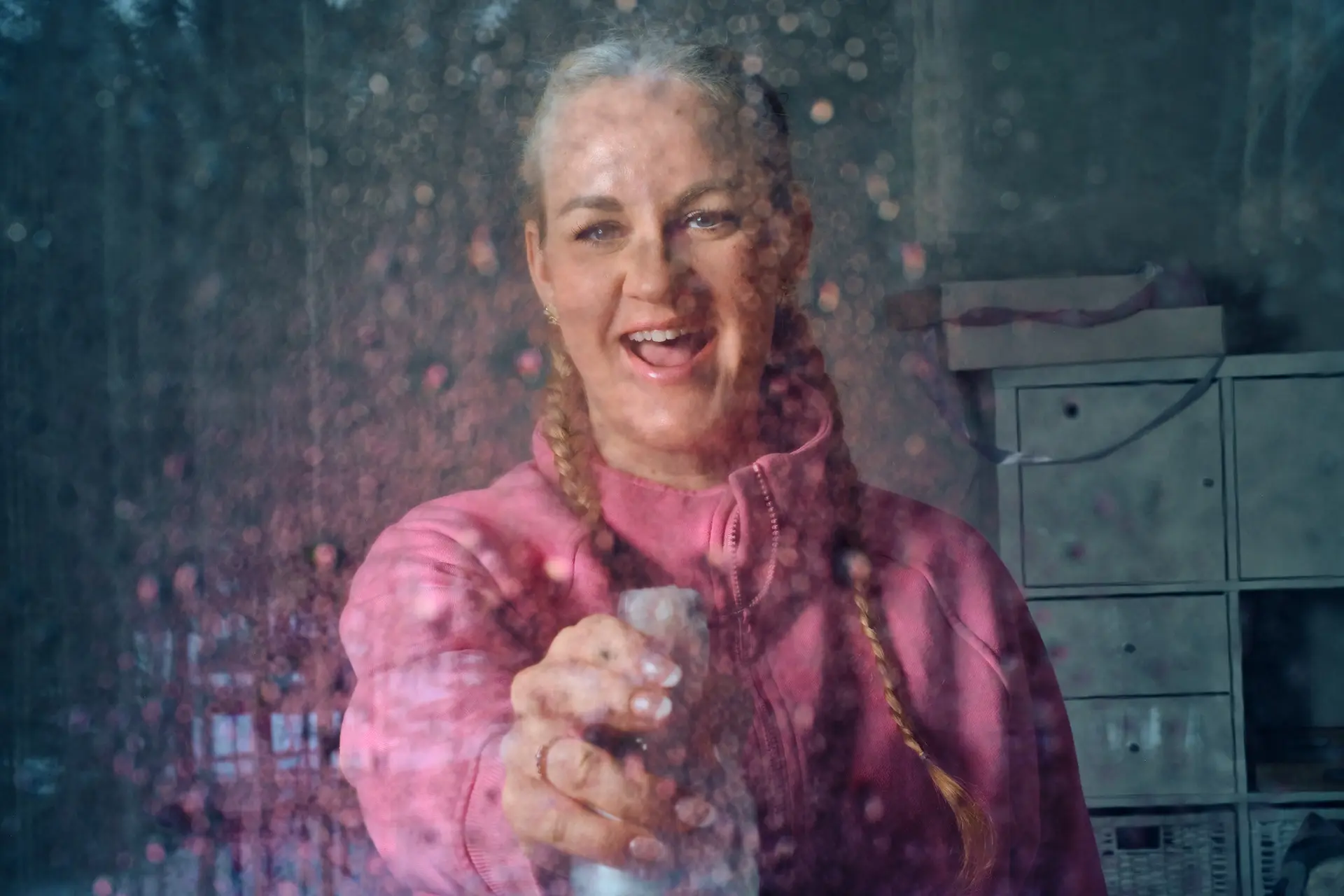 Auri Kananen kuvattuna lasin läpi. Hän suihkuttaa lasiin vettä suihkepullosta.