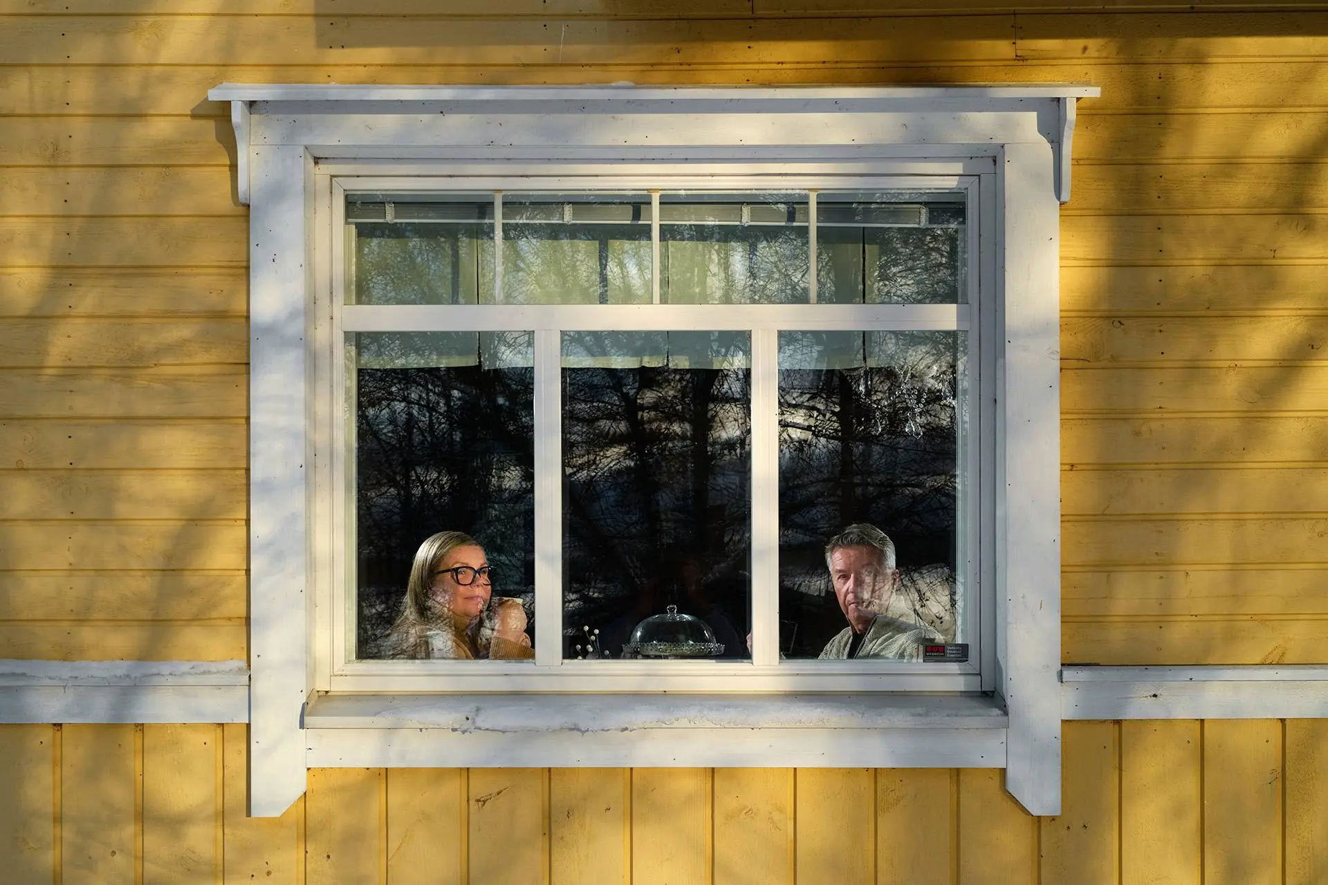 Hirsitalon ikkunoista näkyy Liisa ja Olli kahvipöydän ääressä.