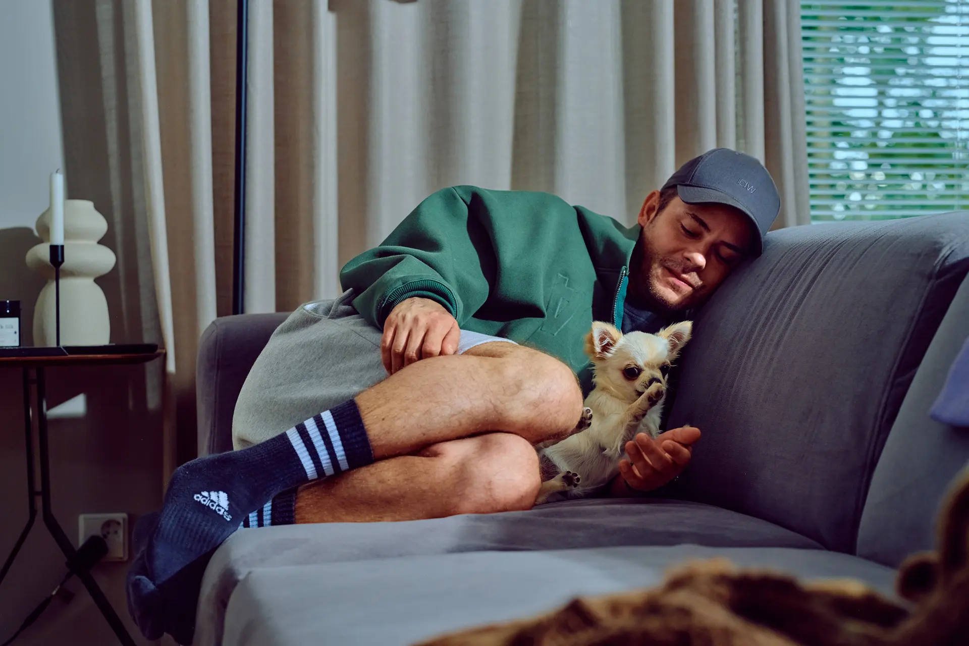 Niko Saarinen on kippurassa sohvannurkassa vieressään vaalea chihuahua. Chihuahua nostaa tassuaan Nikon kädelle.
